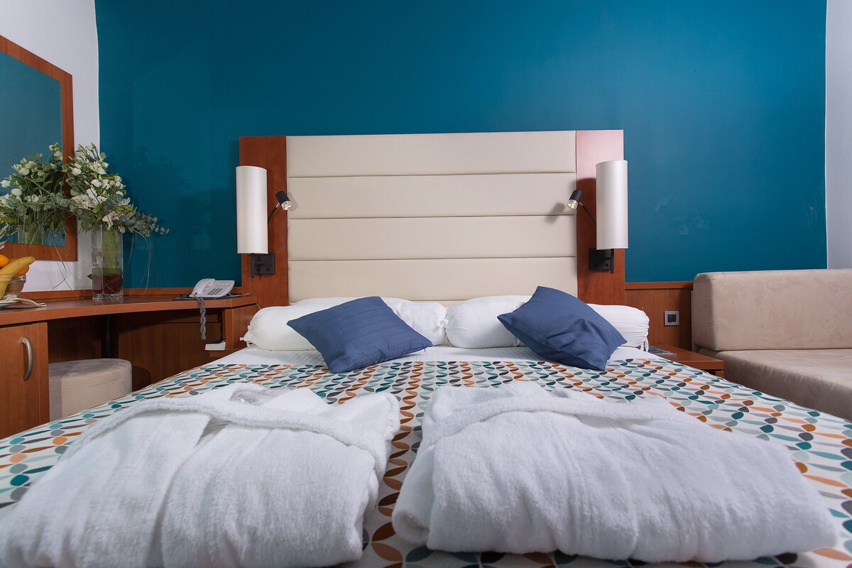 Une chambre d’hôtel avec un lit, un bureau, un téléphone et un vase rempli de fleurs.
