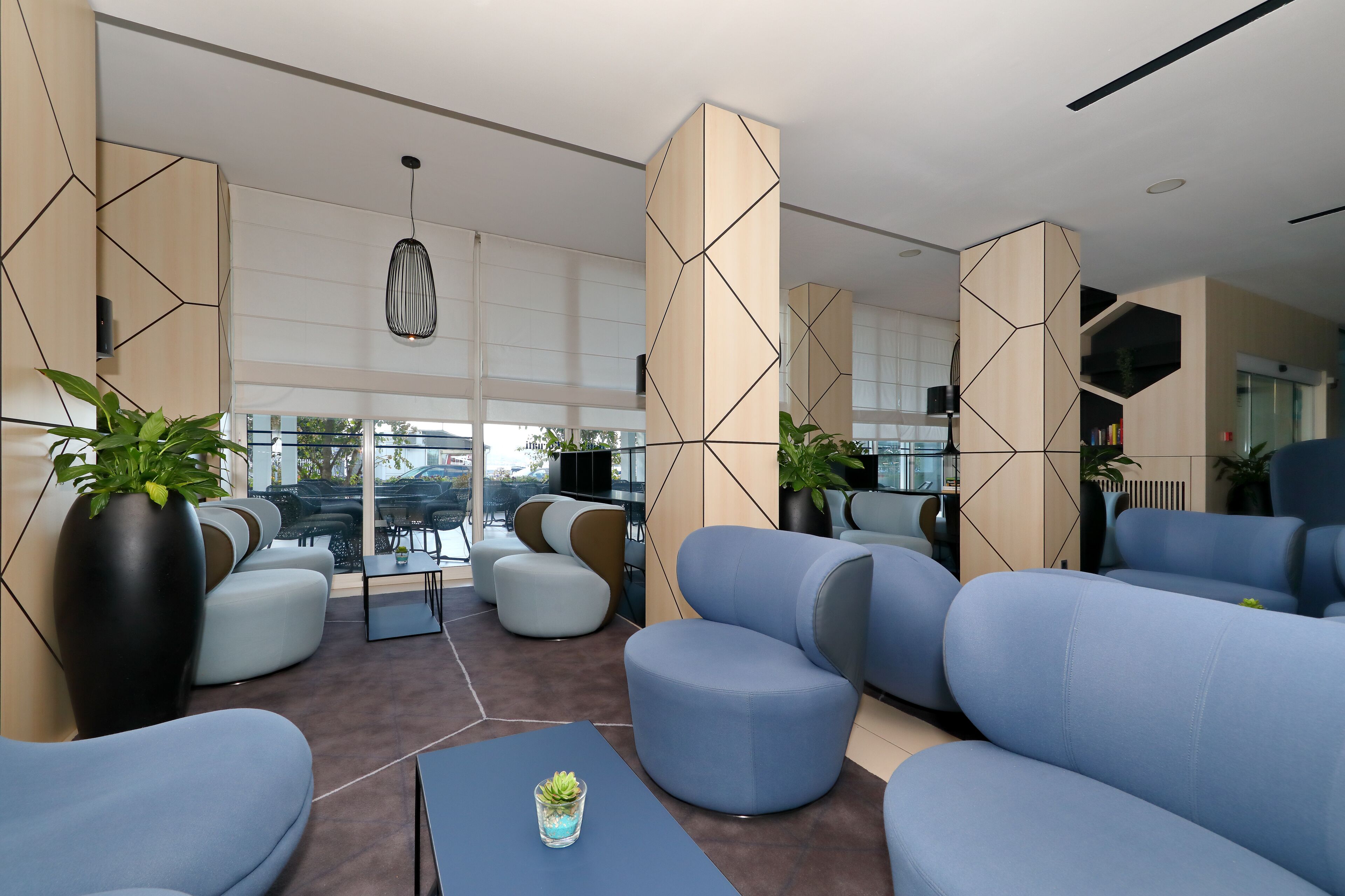 Zona relax moderna con divani blu, una grande pianta in vaso e un tavolino da caffè.