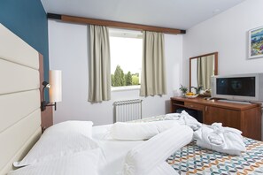 Ein Hotelzimmer mit Bett, Schreibtisch mit Fernseher, Fenster mit Vorhängen und Heizkörper.