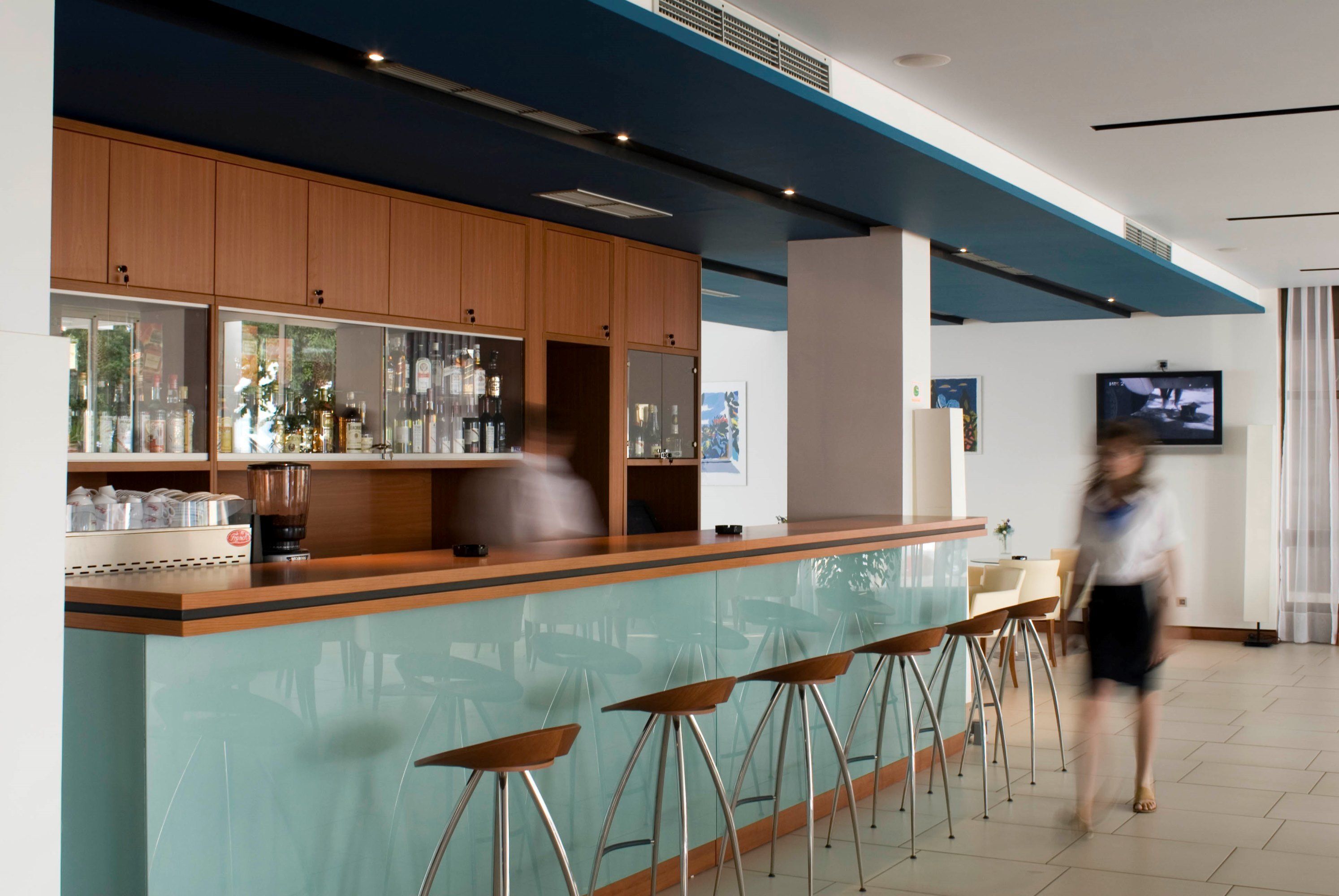 Eine moderne Bar mit einer Glastheke, Holzschränken und Barhocker.