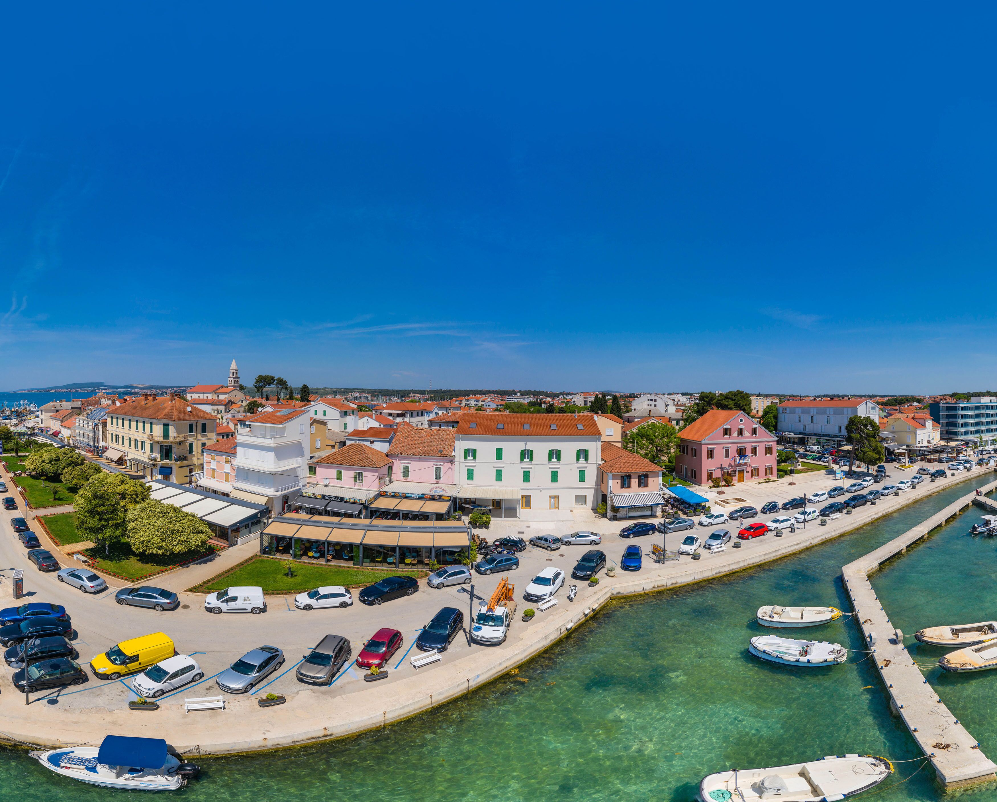 A coastal town with a marina, clear blue sky, and a variety of buildings including a prominent pink structure.