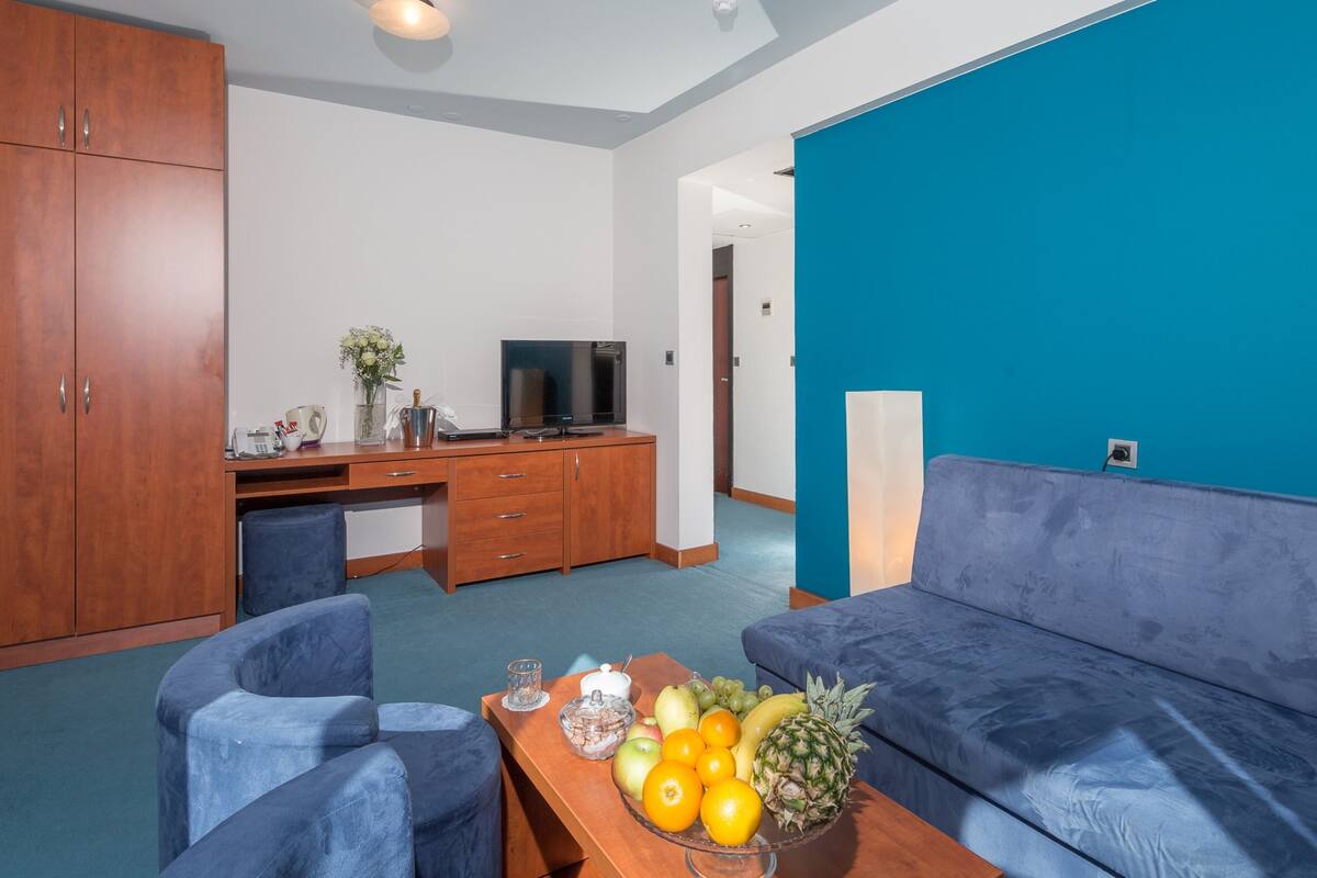Ein modernes Wohnzimmer mit einem blauen Sofa, einem Holztisch und einer Obstschale auf dem Couchtisch.