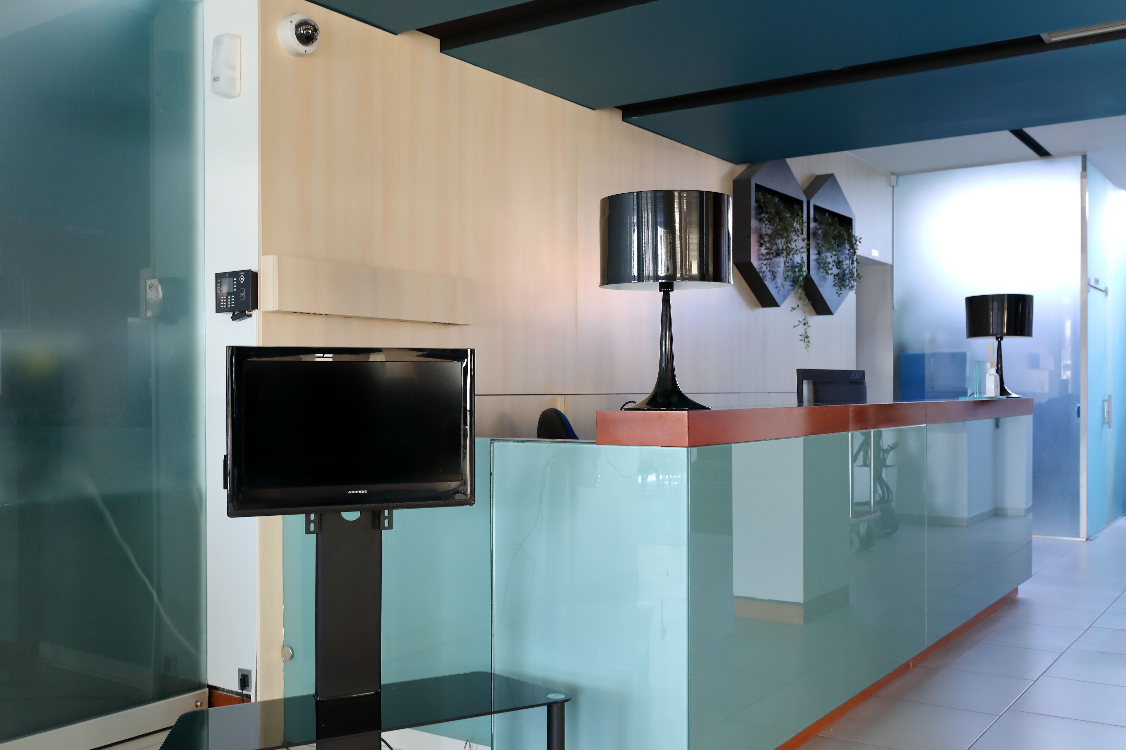 A modern reception area with a glass partition, a flat-screen TV, and a desk with a lamp.