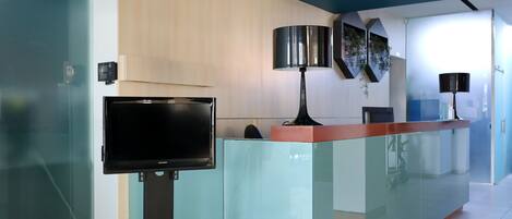 A modern reception area with a glass partition, a flat-screen TV, and a desk with a lamp.