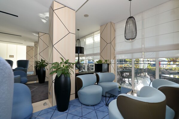 Ein moderner Lounge-Bereich mit Sitzgelegenheiten, großen Fenstern und Topfpflanzen.