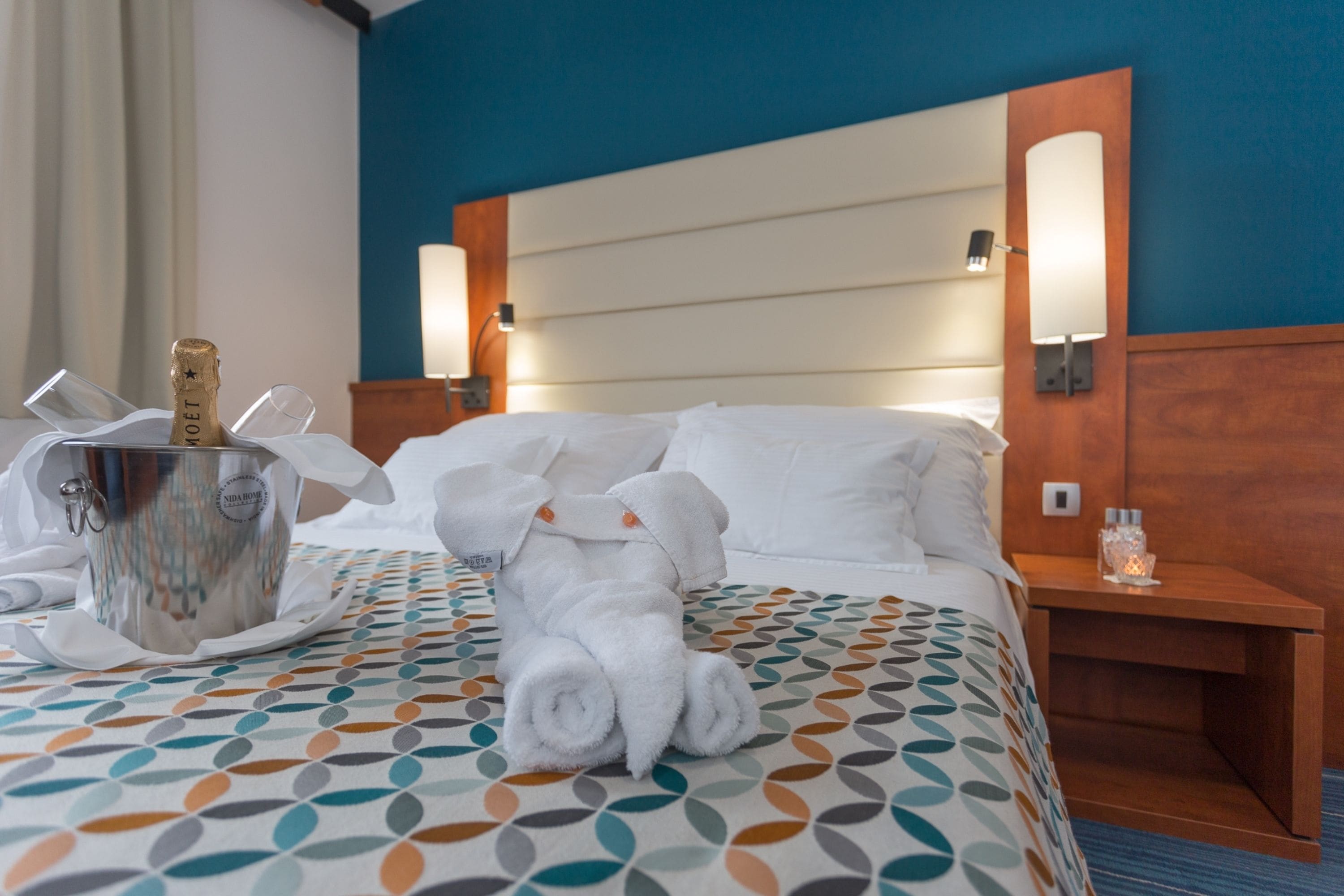 Una camera d'albergo con un letto, un minibar, una bottiglia di champagne e un asciugamano.