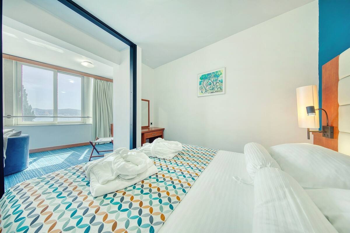Ein Hotelzimmer mit einem großen Bett, einem Schreibtisch, einem Stuhl, einem Vorhangfenster und einem Bild an der Wand.