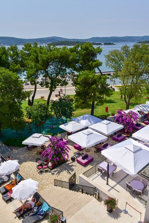 An outdoor seating area with umbrellas, lounge chairs, and a view of the sea. - Hotel Kornati Biograd (Biograd na Moru)