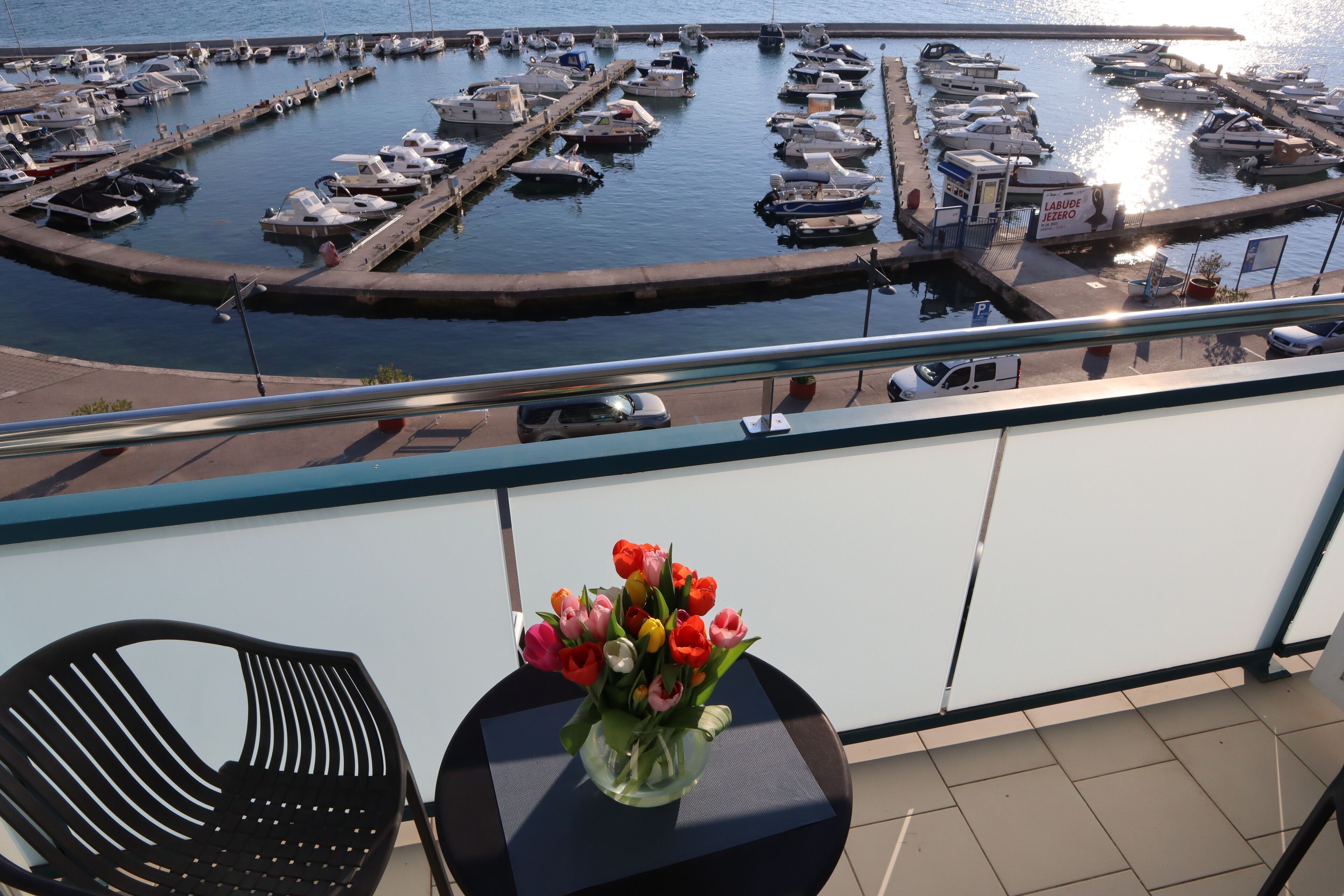 A balcony with a table and a vase of flowers, overlooking a marina with boats.
