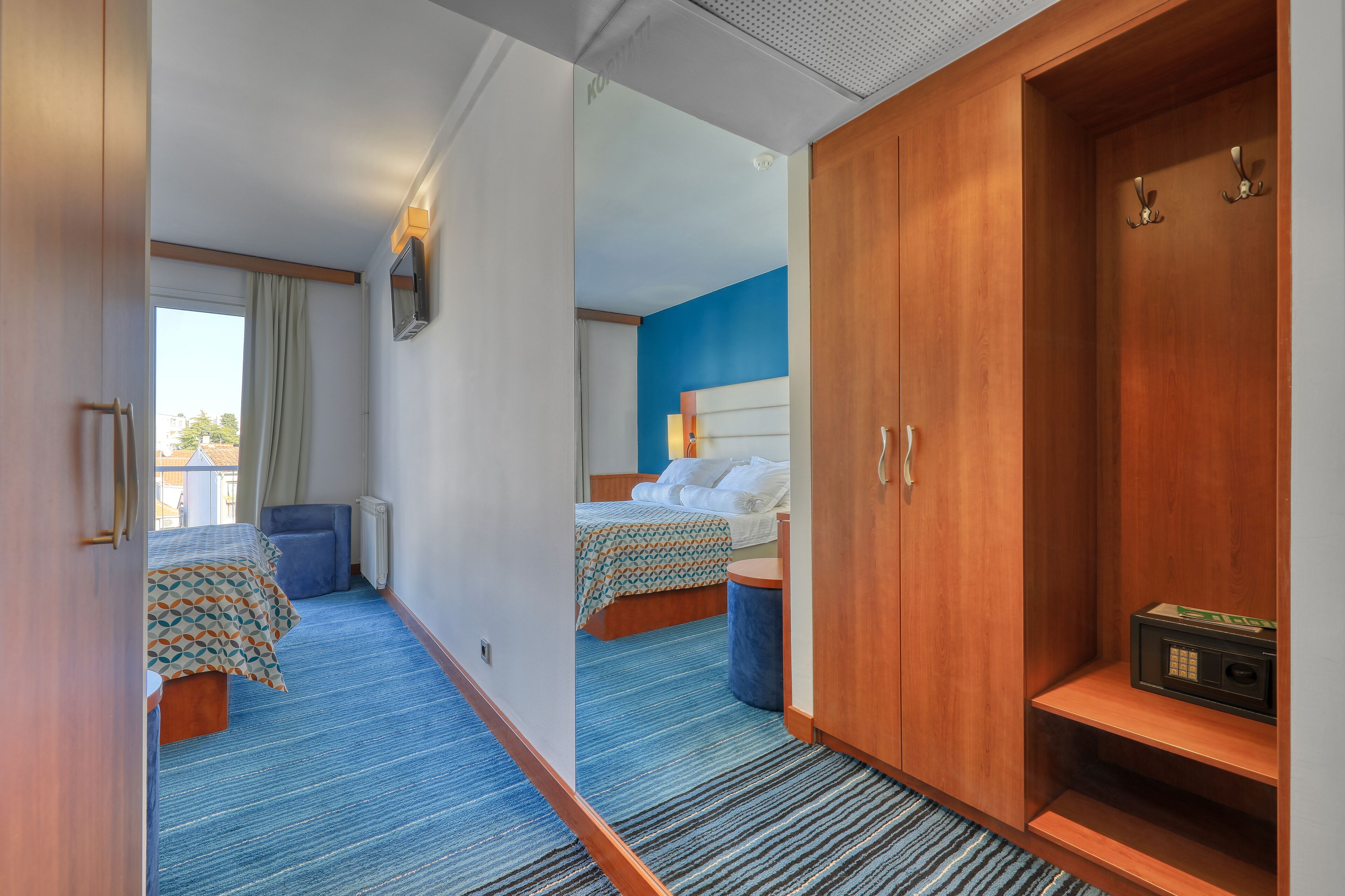 A hotel room with a bed, a wardrobe, a desk, and a window with curtains.