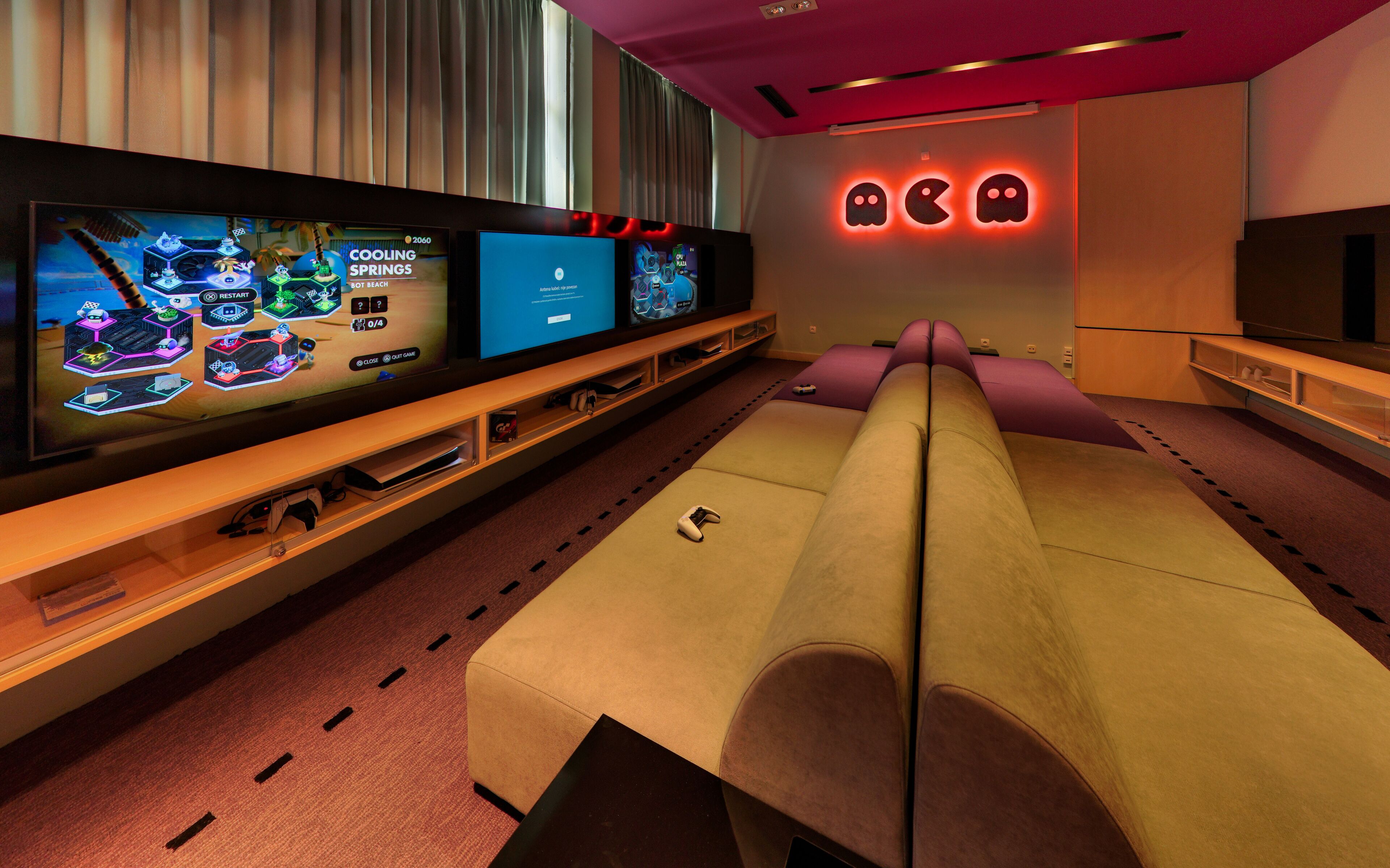 Een moderne gamekamer met twee grote flatscreen televisies die games tonen, een comfortabele bank en een neonreclame op de muur.