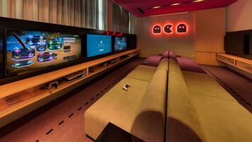 Een moderne gamekamer met twee grote flatscreen televisies die games tonen, een comfortabele bank en een neonreclame op de muur.
