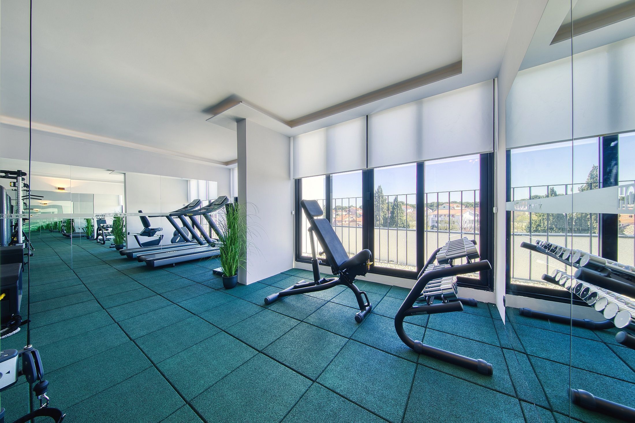 Un gimnasio moderno con equipamiento de ejercicio, amplias ventanas y vistas a la ciudad.