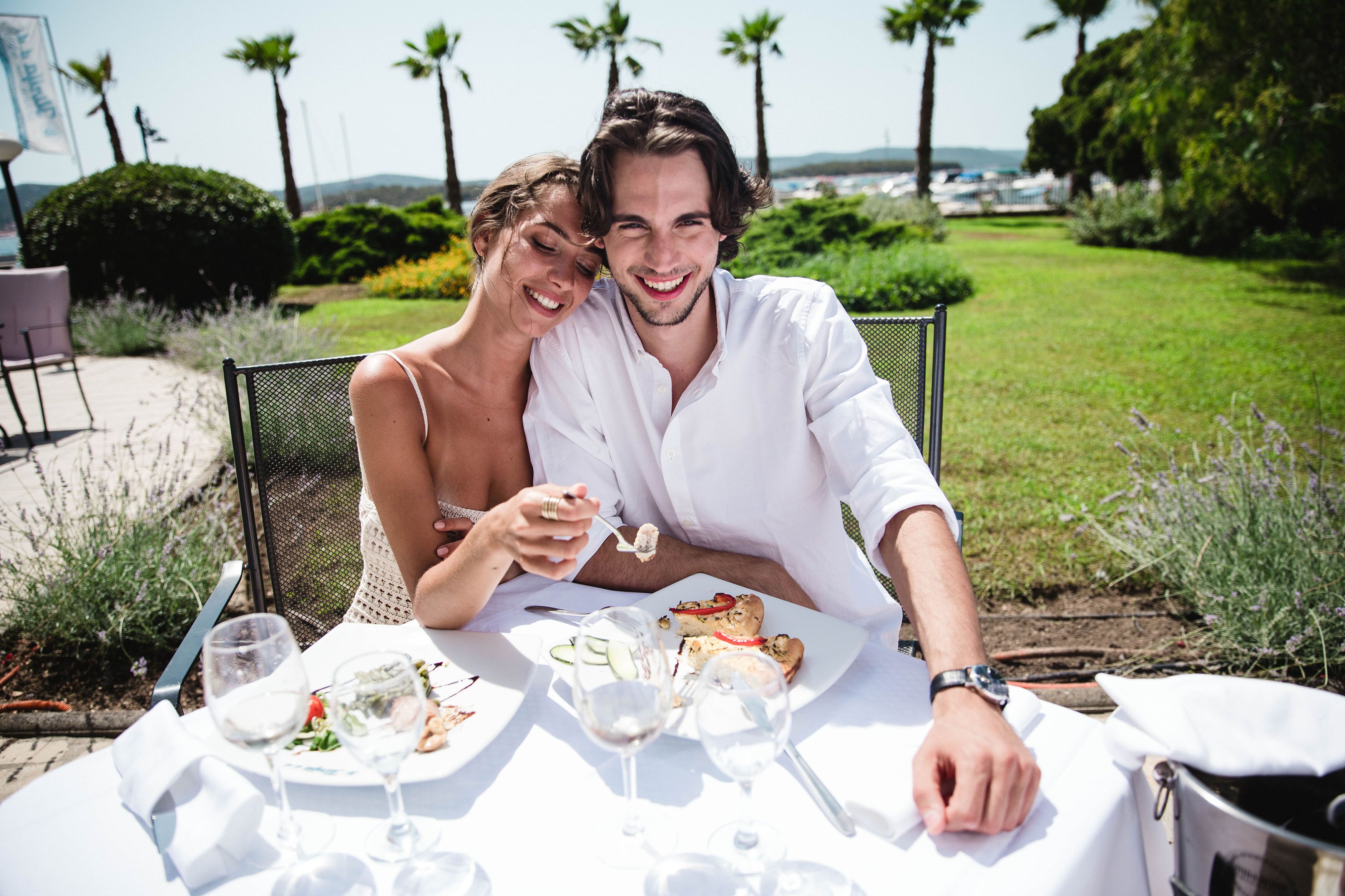 Una pareja cenando al aire libre en una mesa para dos, rodeada de vegetación y palmeras.