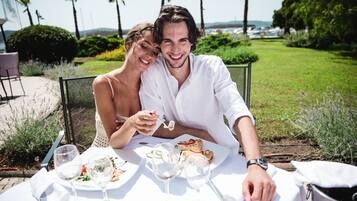 Una pareja cenando al aire libre en una mesa para dos, rodeada de vegetación y palmeras.