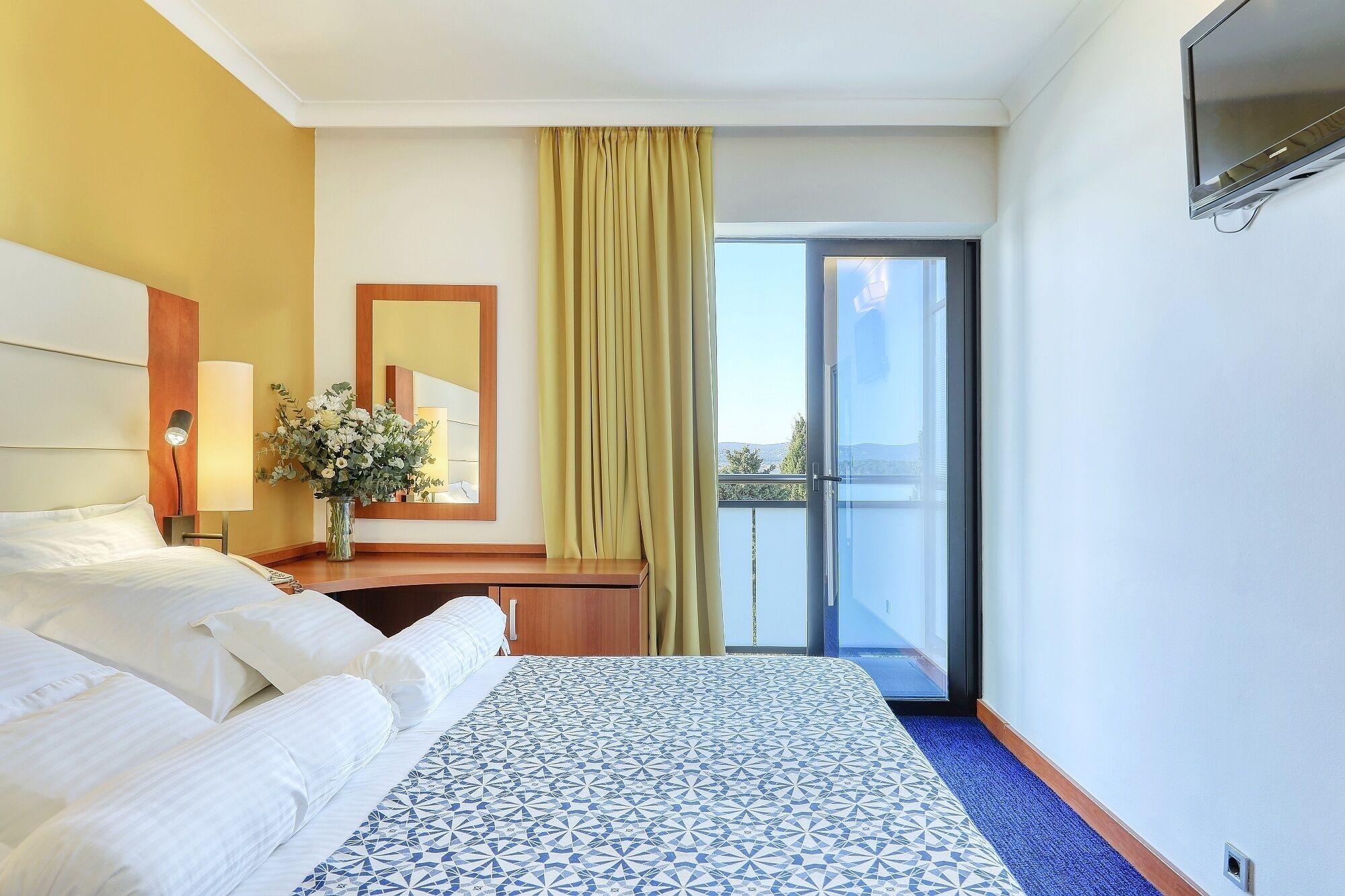 Une chambre d’hôtel comprenant un lit, un bureau, un miroir, une fenêtre avec des rideaux et une vue sur l’extérieur.
