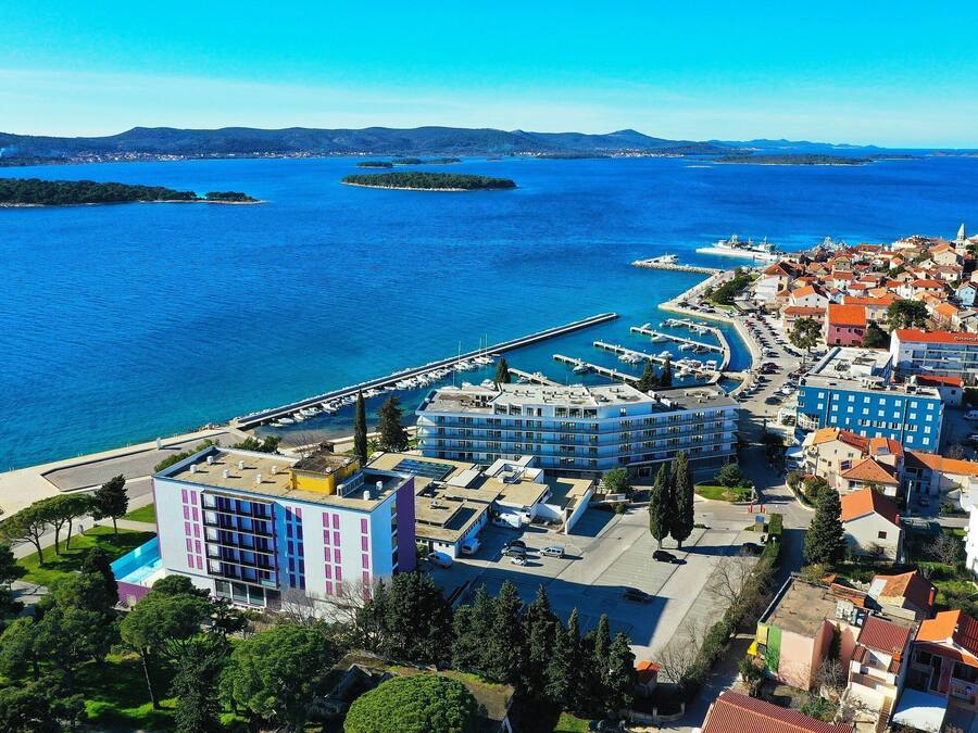 A coastal town with a marina, buildings with red roofs, and a pier extending into the water.