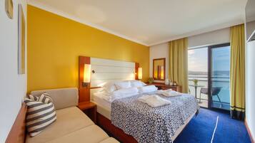 A hotel room with a bed, a sofa, a small table with a chair, and a balcony with a view.