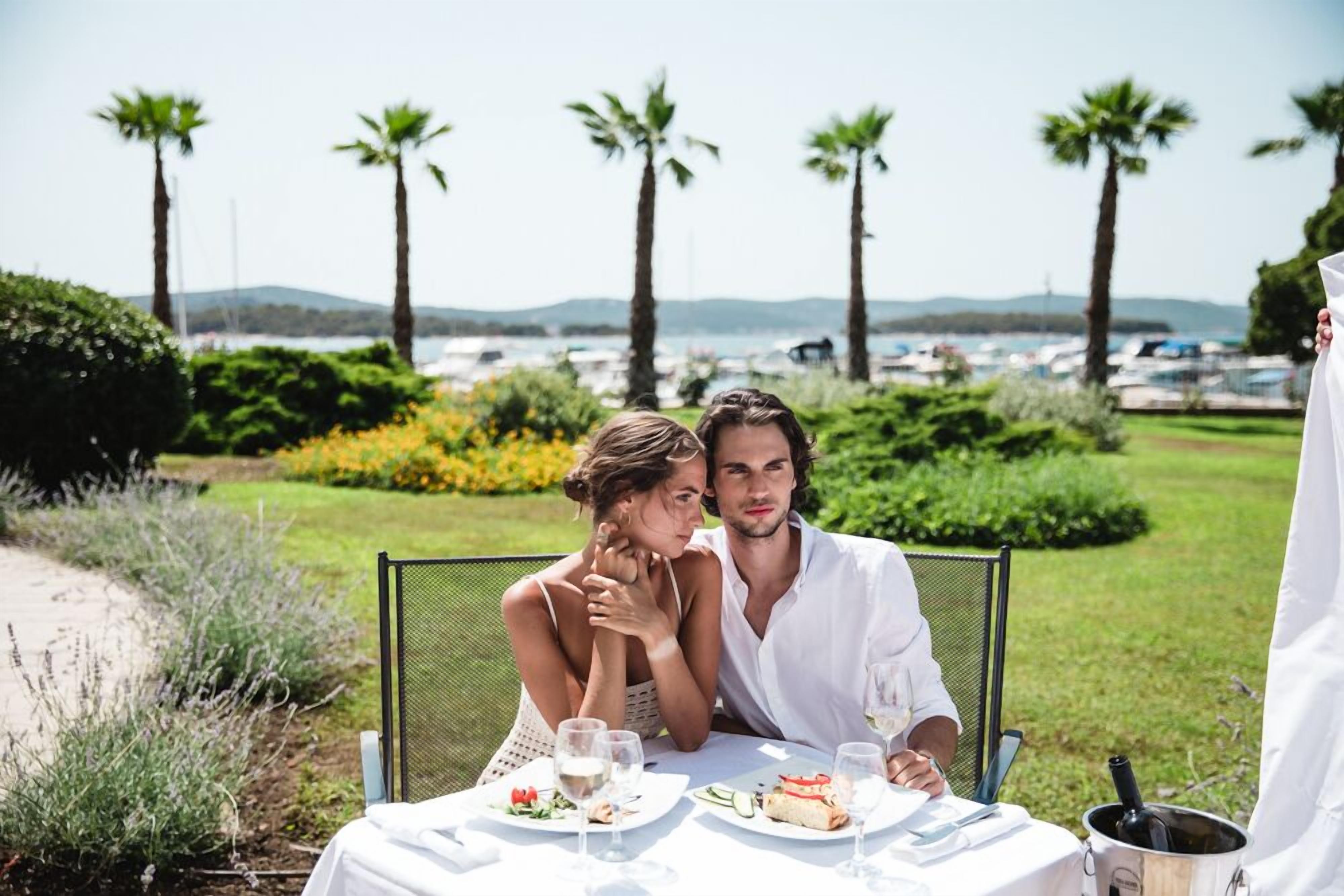 A couple dining outdoors with a view of the sea and boats.