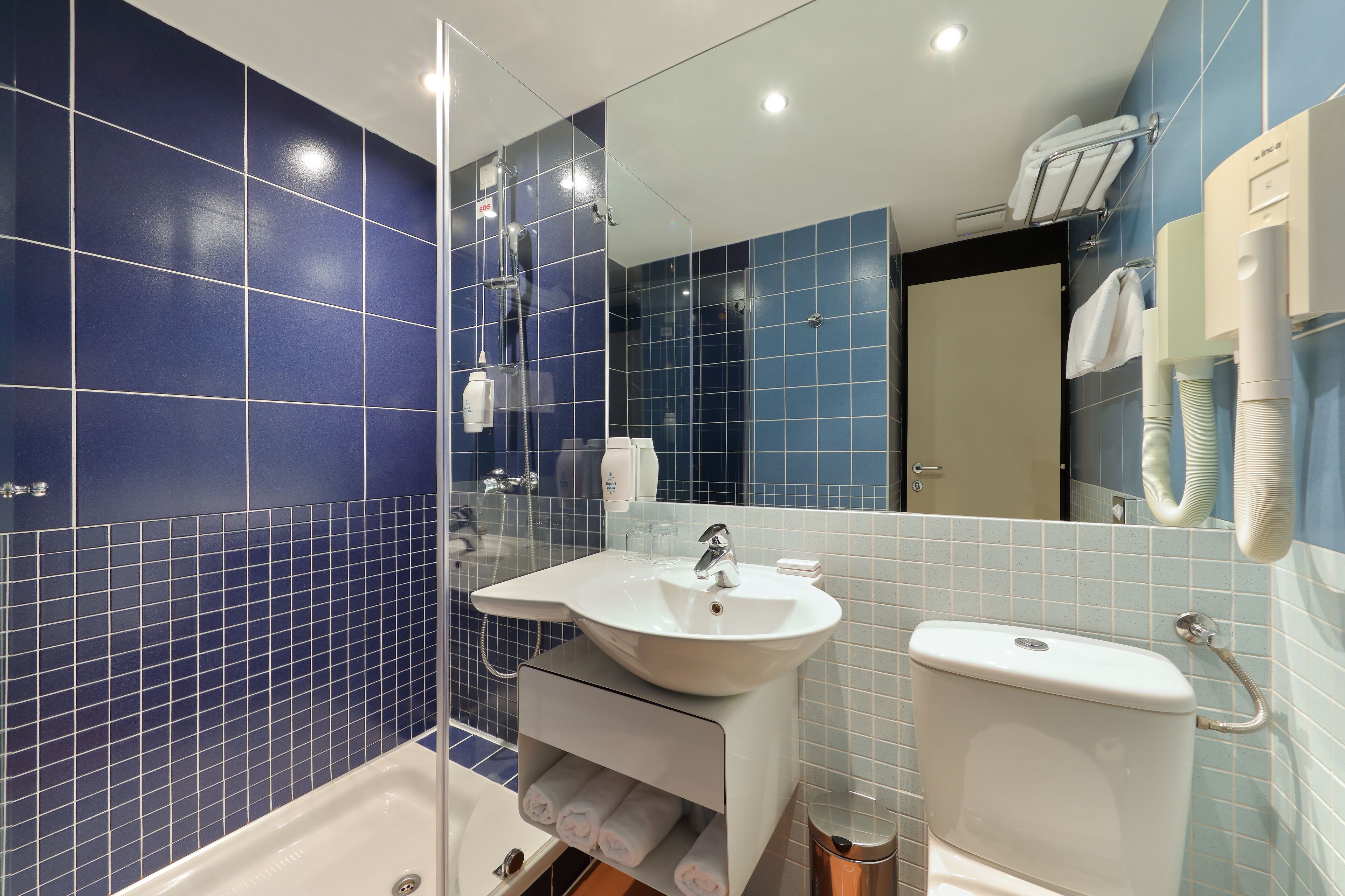 Un baño moderno con azulejos azules, un lavamanos blanco y una bañera.