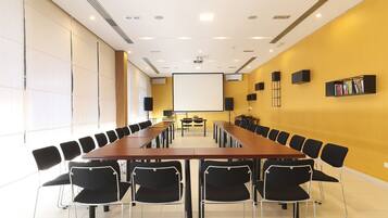 A conference room with a long table, black chairs, a projector screen, and a bookshelf.