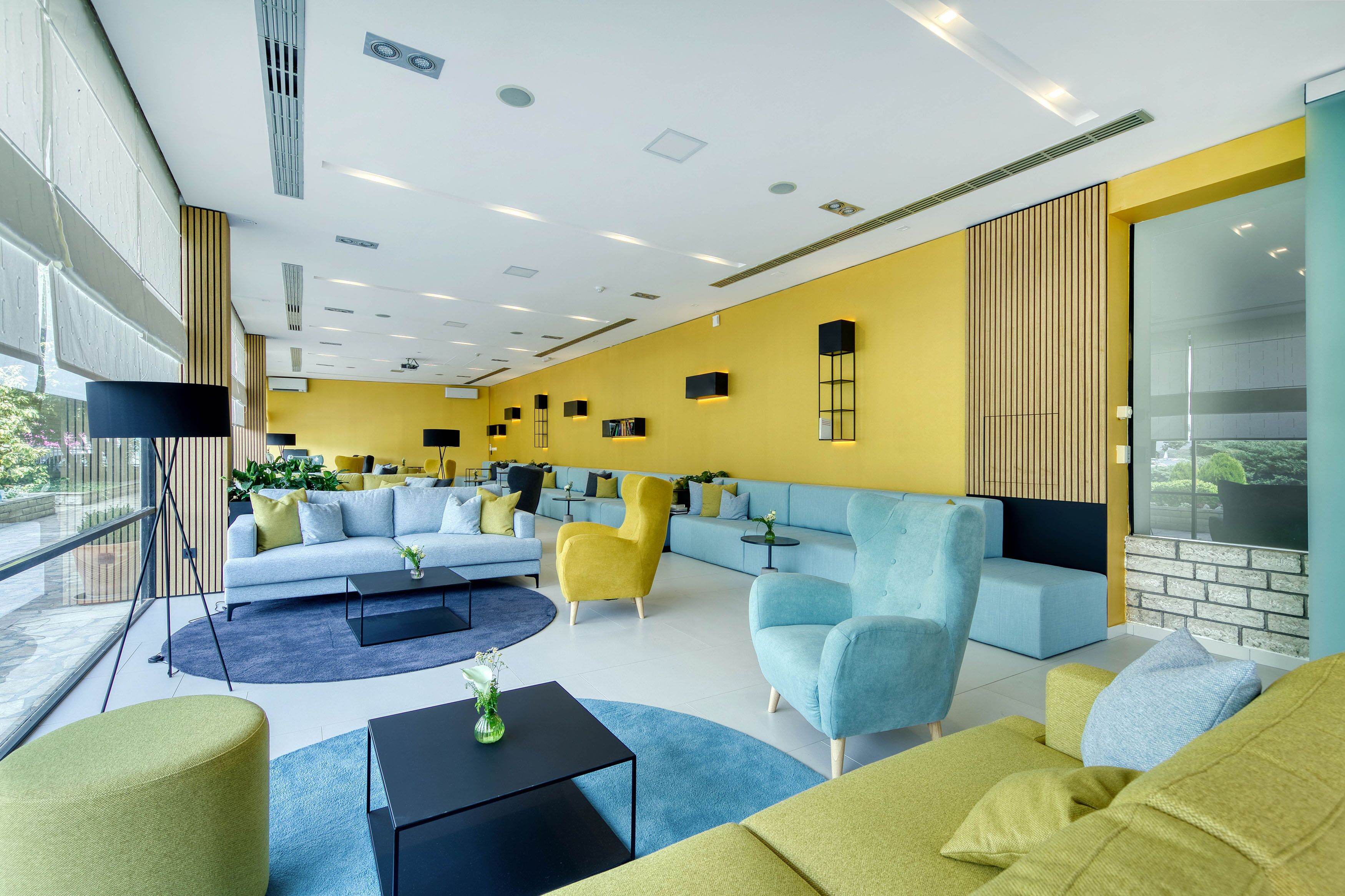 A modern lounge area with sofas and armchairs, a coffee table, and a large window providing a view of the outdoors.
