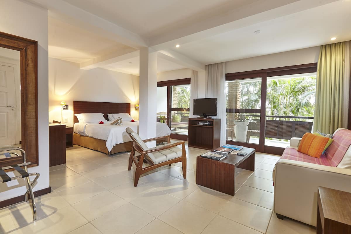 A hotel room with a bed, a sofa, a TV, a desk, and a balcony with a view.
