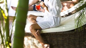 A couple relaxing on a wicker bed with a canopy, surrounded by greenery. - PortoBay Búzios (Búzios)