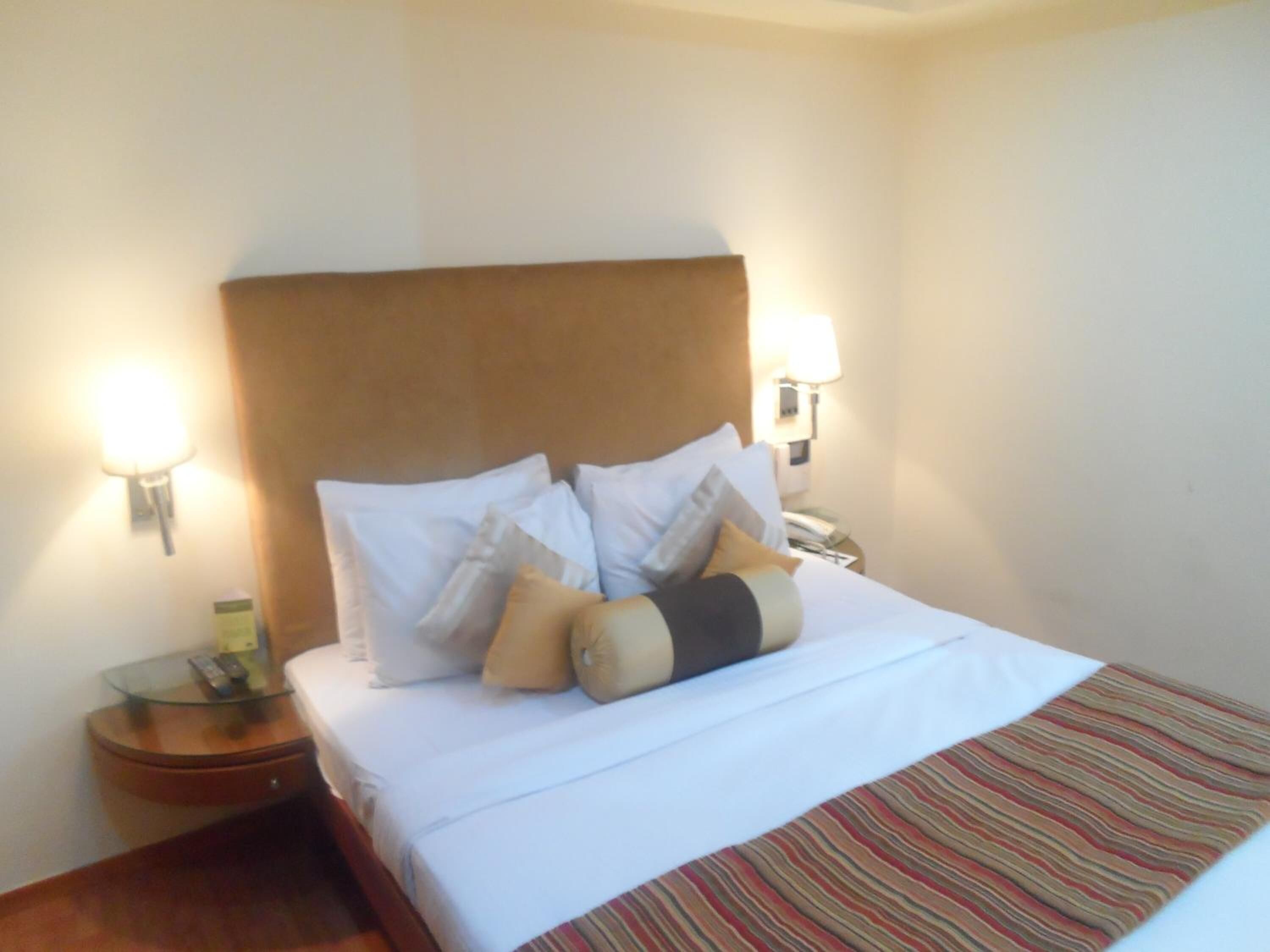 A hotel room with a large bed, two bedside lamps, a nightstand with a phone, and a striped throw blanket.