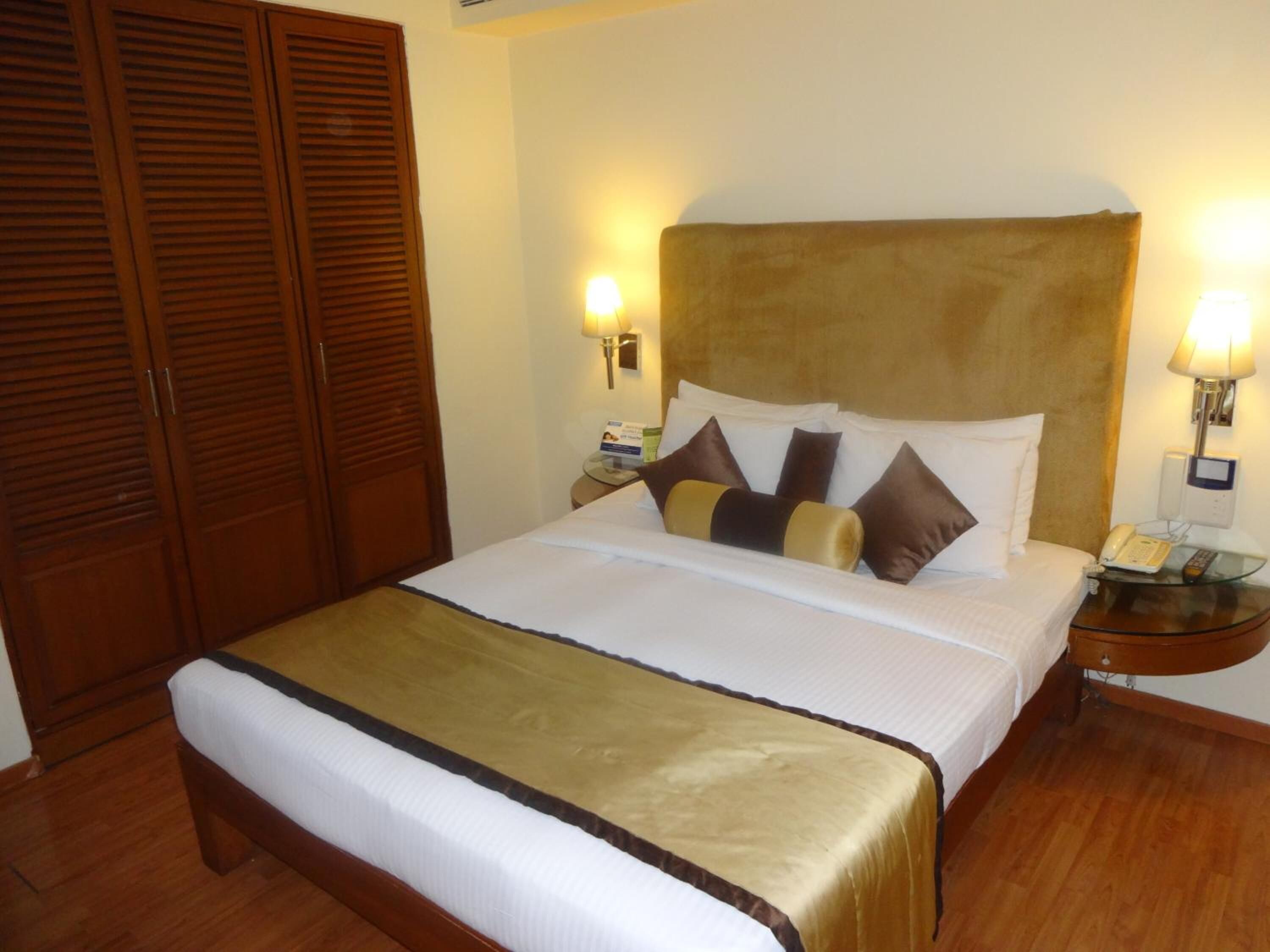 Habitación de hotel con una cama grande, un armario de madera, mesitas de noche con lámparas y un teléfono.