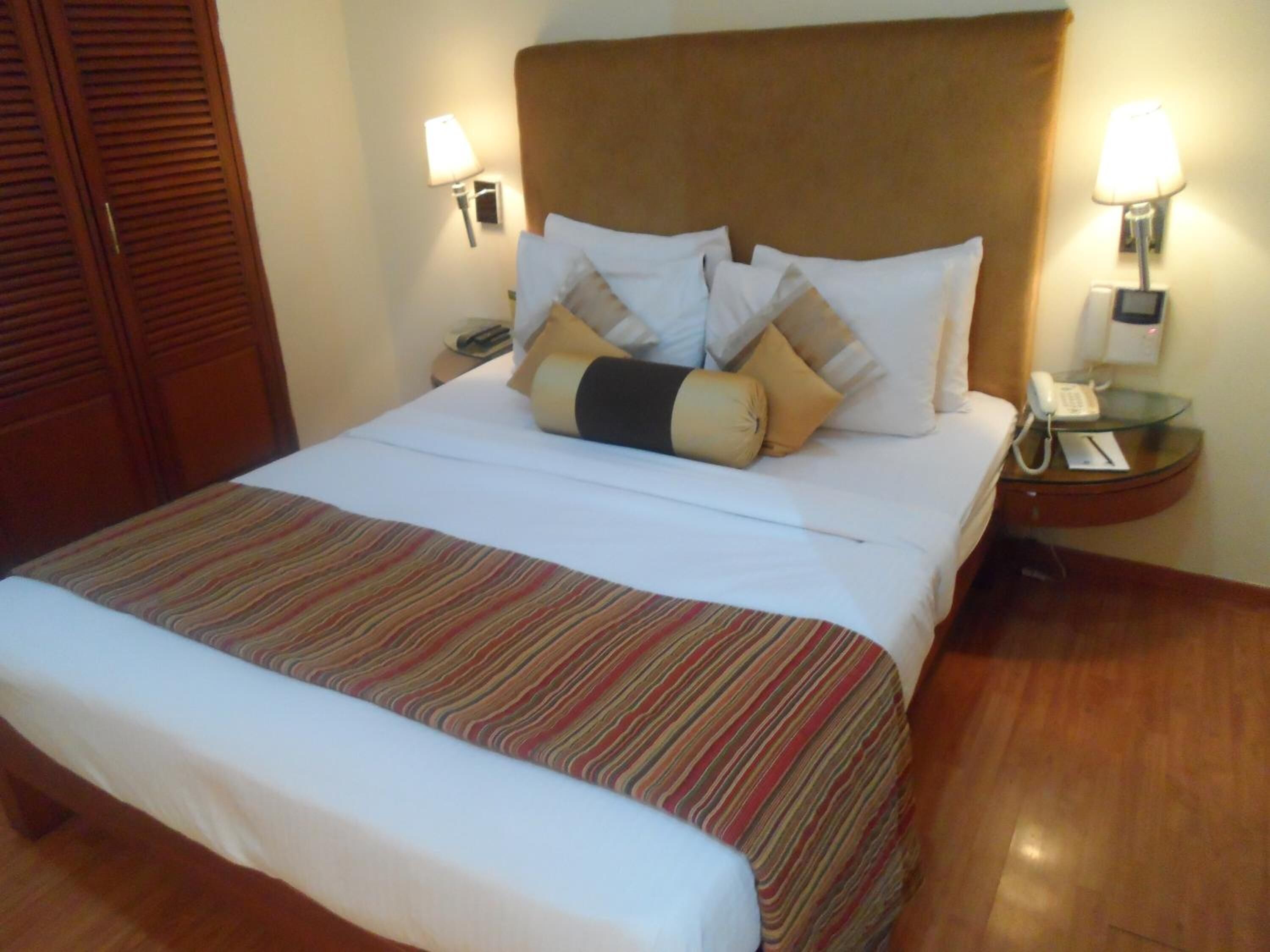 A hotel room with a large bed, striped bedspread, two bedside tables with lamps, a telephone, and a wooden wardrobe.