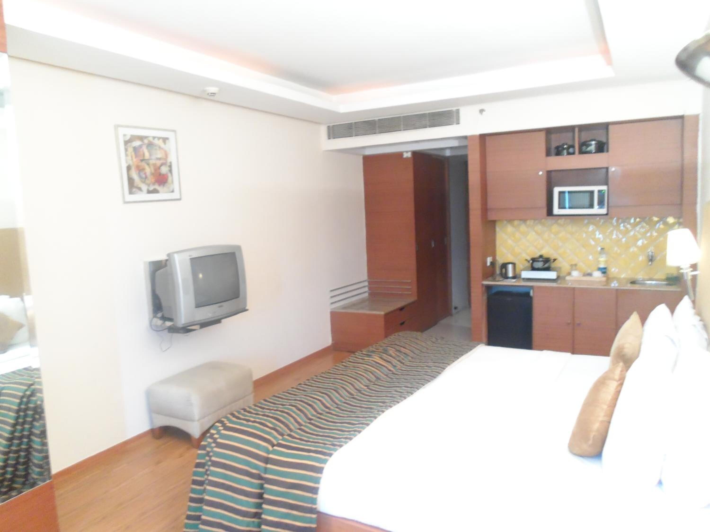 Una habitación de hotel con cama, televisión, kitchenette pequeña y baño.