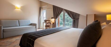 A hotel room with a bed, a sofa, a small table with a lamp, and a window with curtains.
