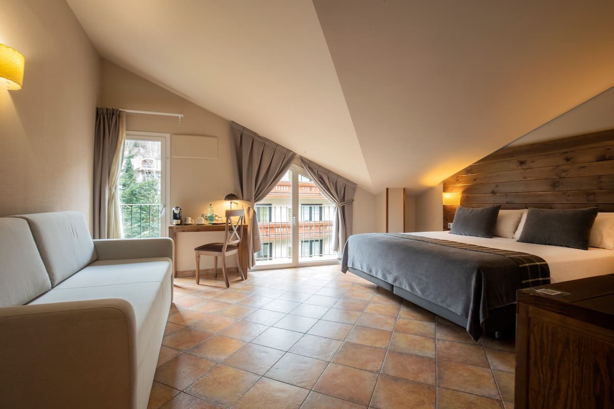 A bedroom with a bed, a sofa, a desk, and a view of the outside.