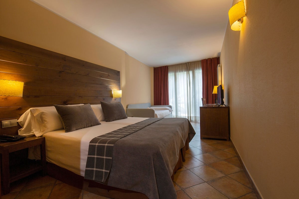 A hotel room with a large bed, a smaller bed, a nightstand, a desk, and a lamp.