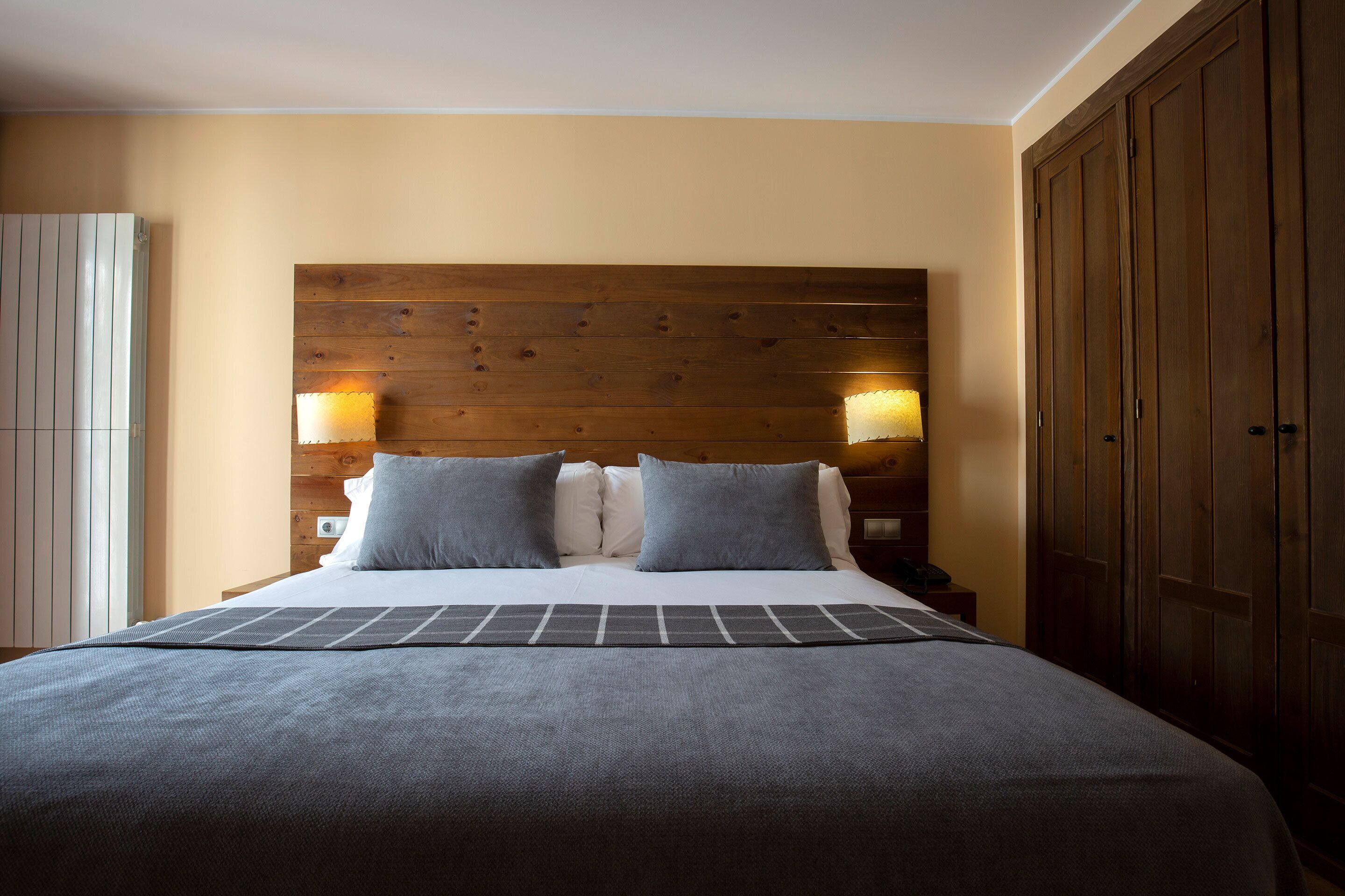 Ein ordentlich gemachtes Bett mit einem Holz-Kopfteil, zwei Nachttischlampen und einem großen Kleiderschrank.