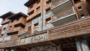 Un edificio de varios pisos con fachada de madera y detalles de piedra, que cuenta con balcones y un letrero que dice "LE NEVADA".