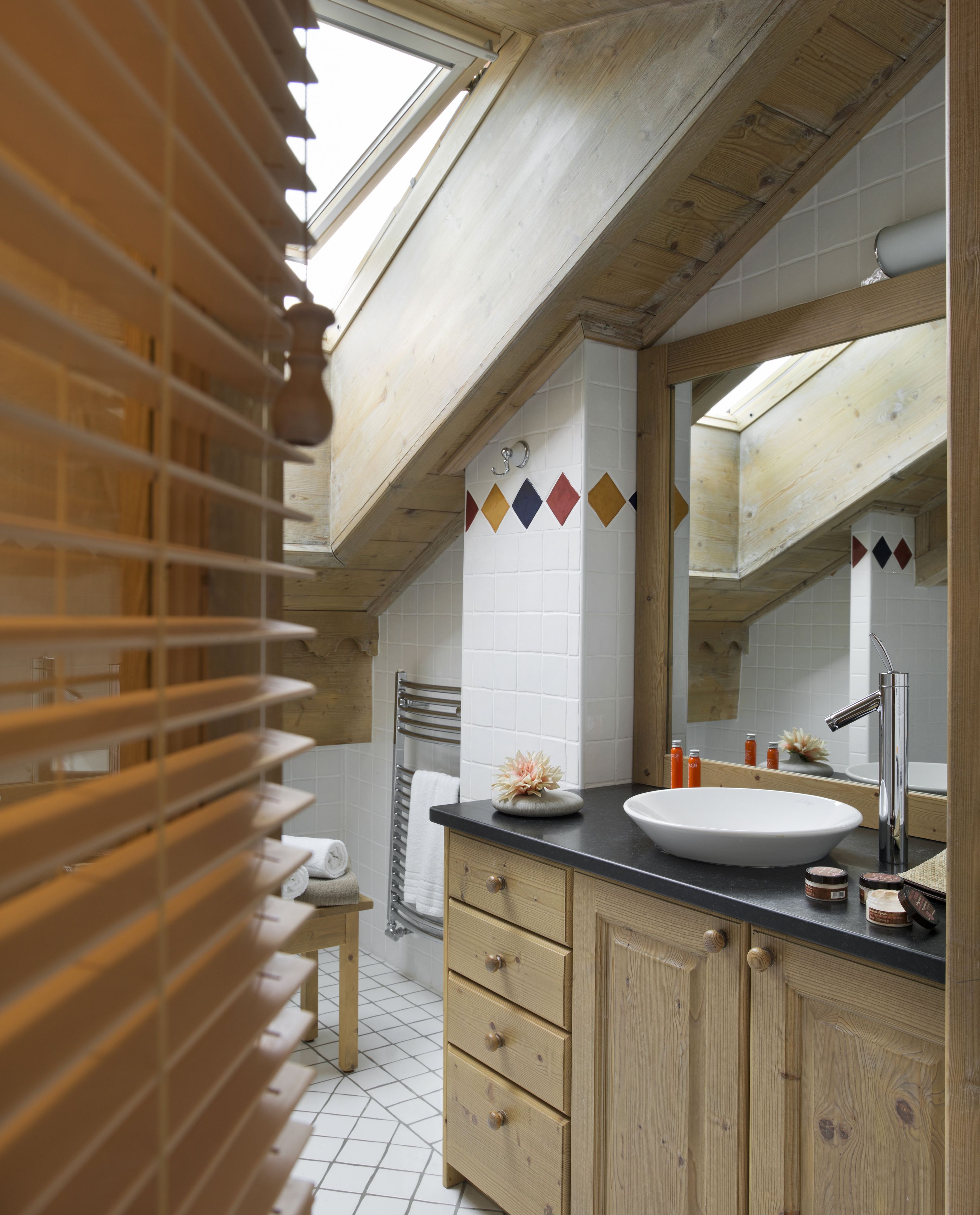 A modern bathroom with a skylight, wooden beams, a large mirror, and a white sink.