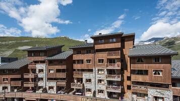 Un edificio in legno a più piani con balconi e dettagli in pietra, probabilmente un hotel o un resort, con una vista chiara sulle montagne sullo sfondo.