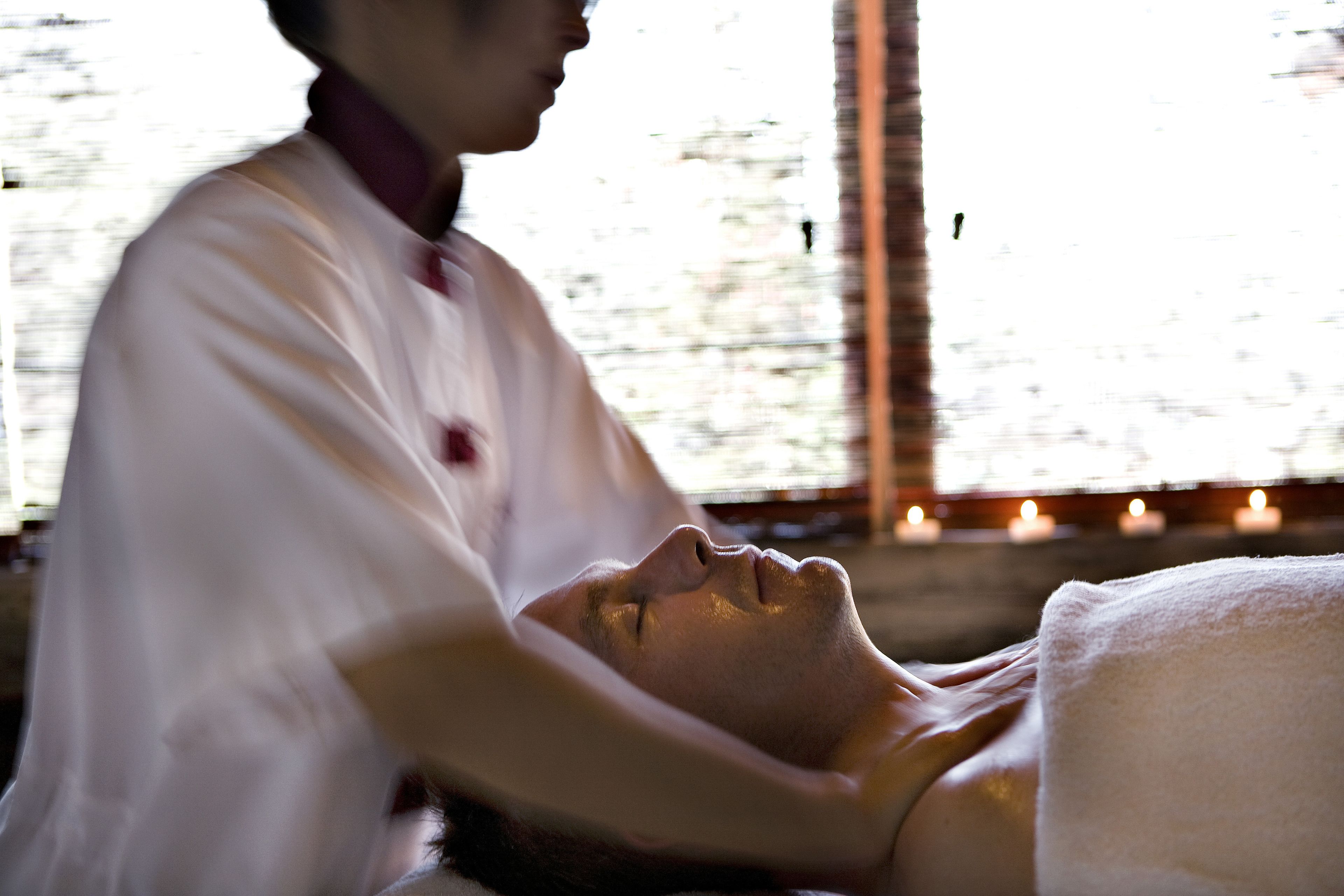 En massagebehandling i et rum med stort vindue og stearinlys.