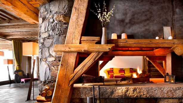 Una acogedora zona con chimenea, pared de piedra, vigas de madera y un conjunto de asientos confortable.