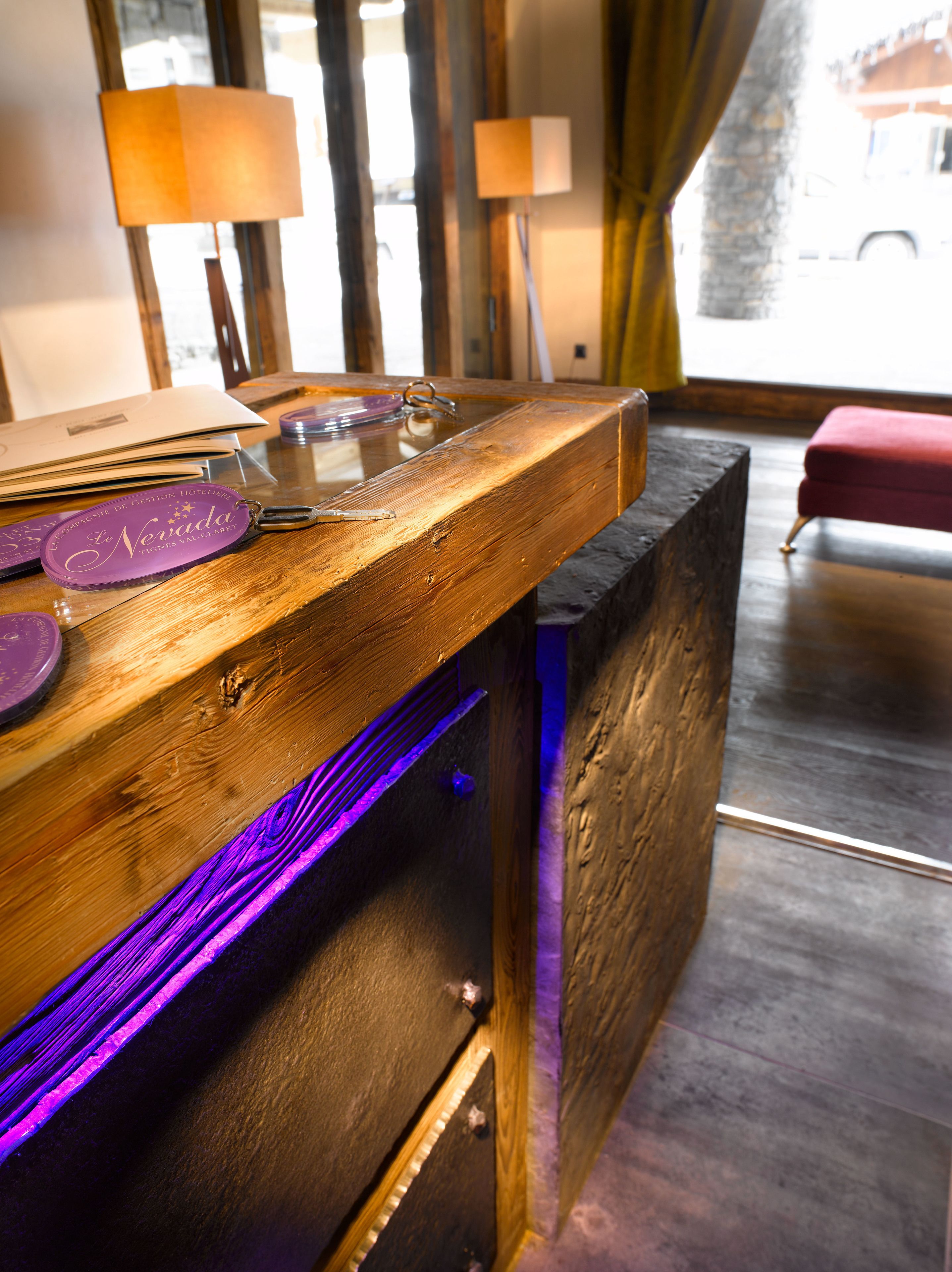 Un mostrador de recepción de madera con cubierta de vidrio, un llavero morado y una lámpara al fondo.