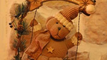 Een teddybeer op een schommel met een 'WELCOME' bord, omringd door dennenappels en een kleine kerstboom.