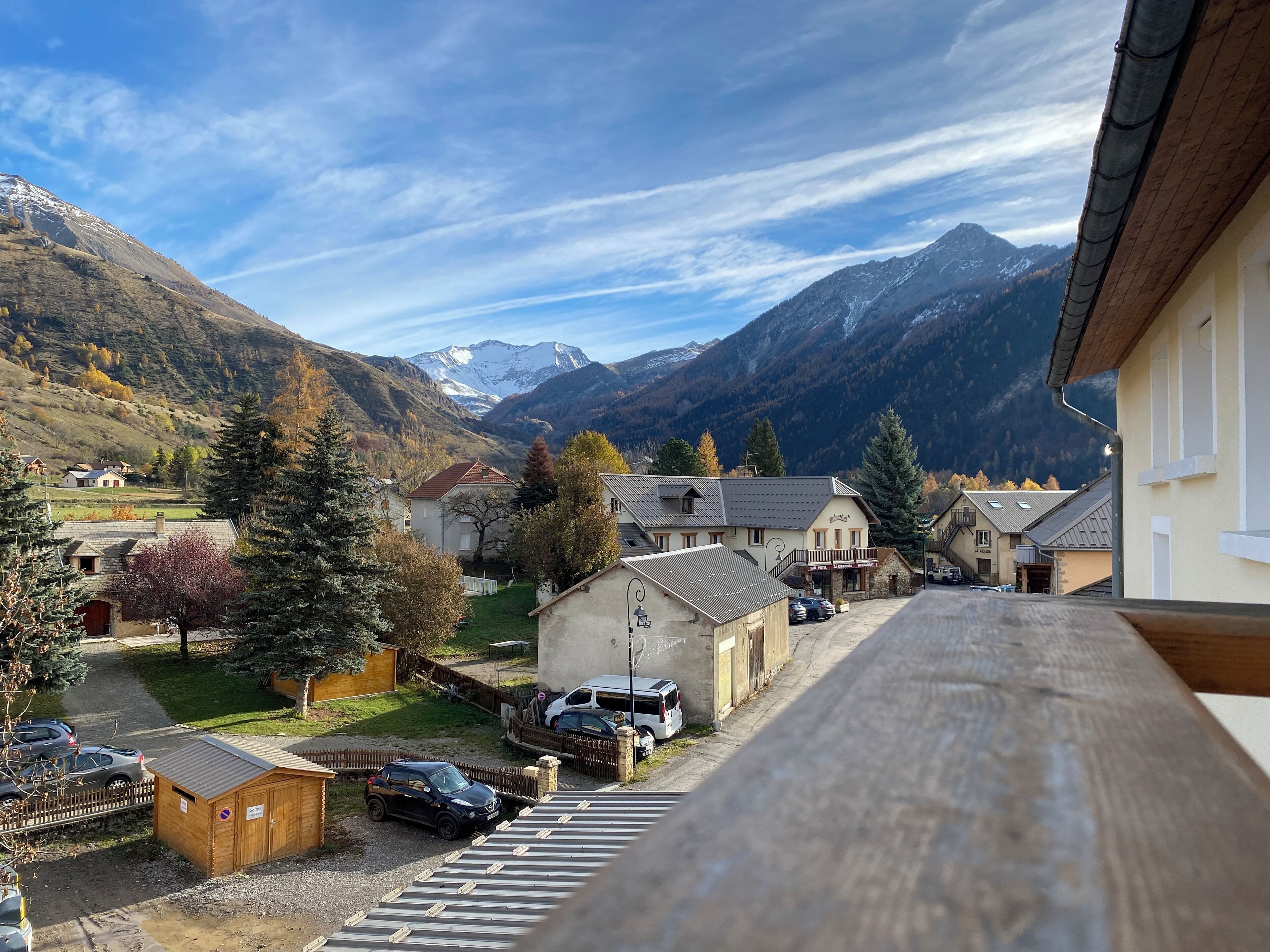 A mountain village with traditional buildings, a parking area, and a view of snow-capped mountains.