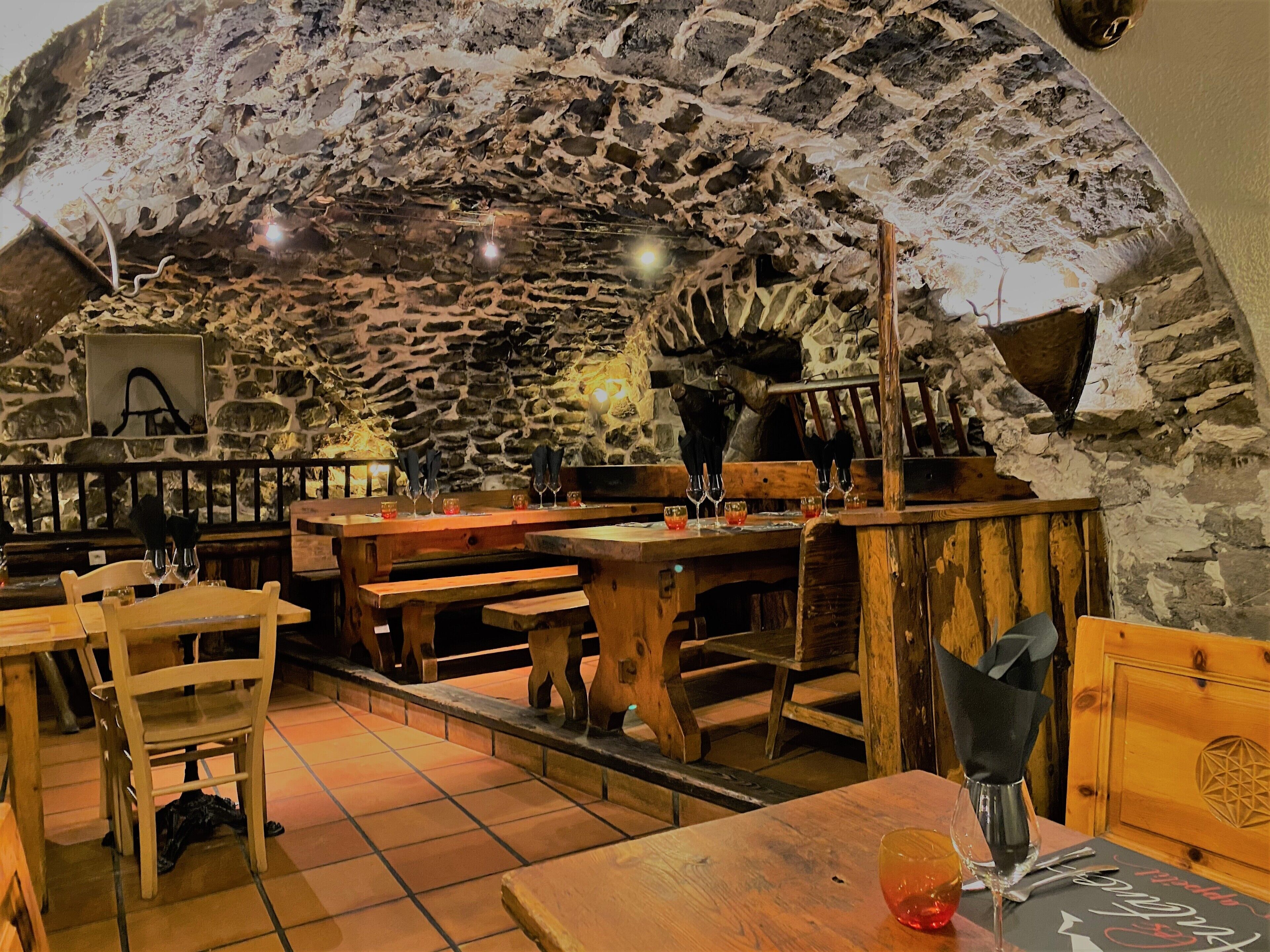 A rustic interior with stone walls, wooden benches, and tables set for dining.