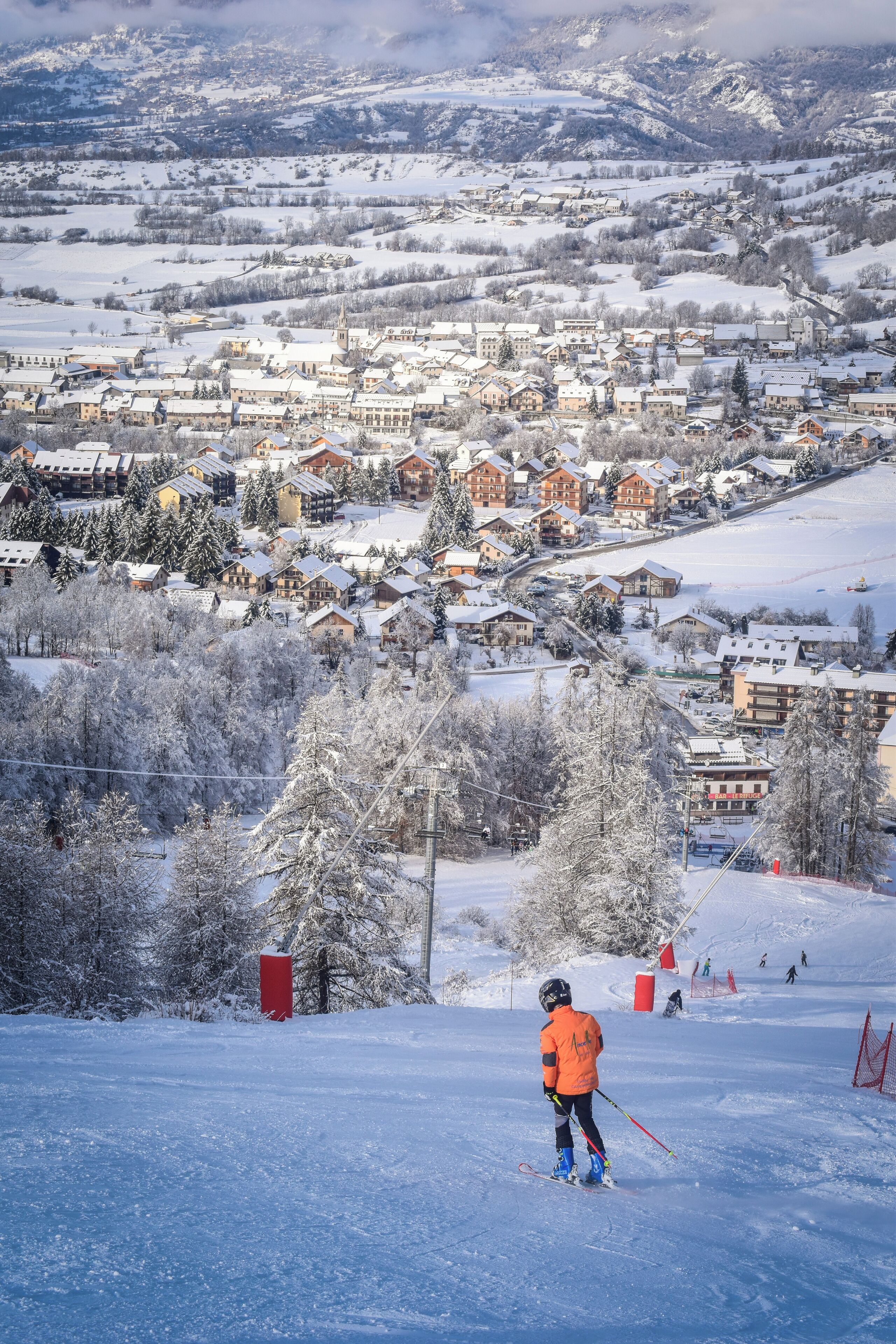 Une station de ski avec des bâtiments recouverts de neige et un skieur sur la piste.