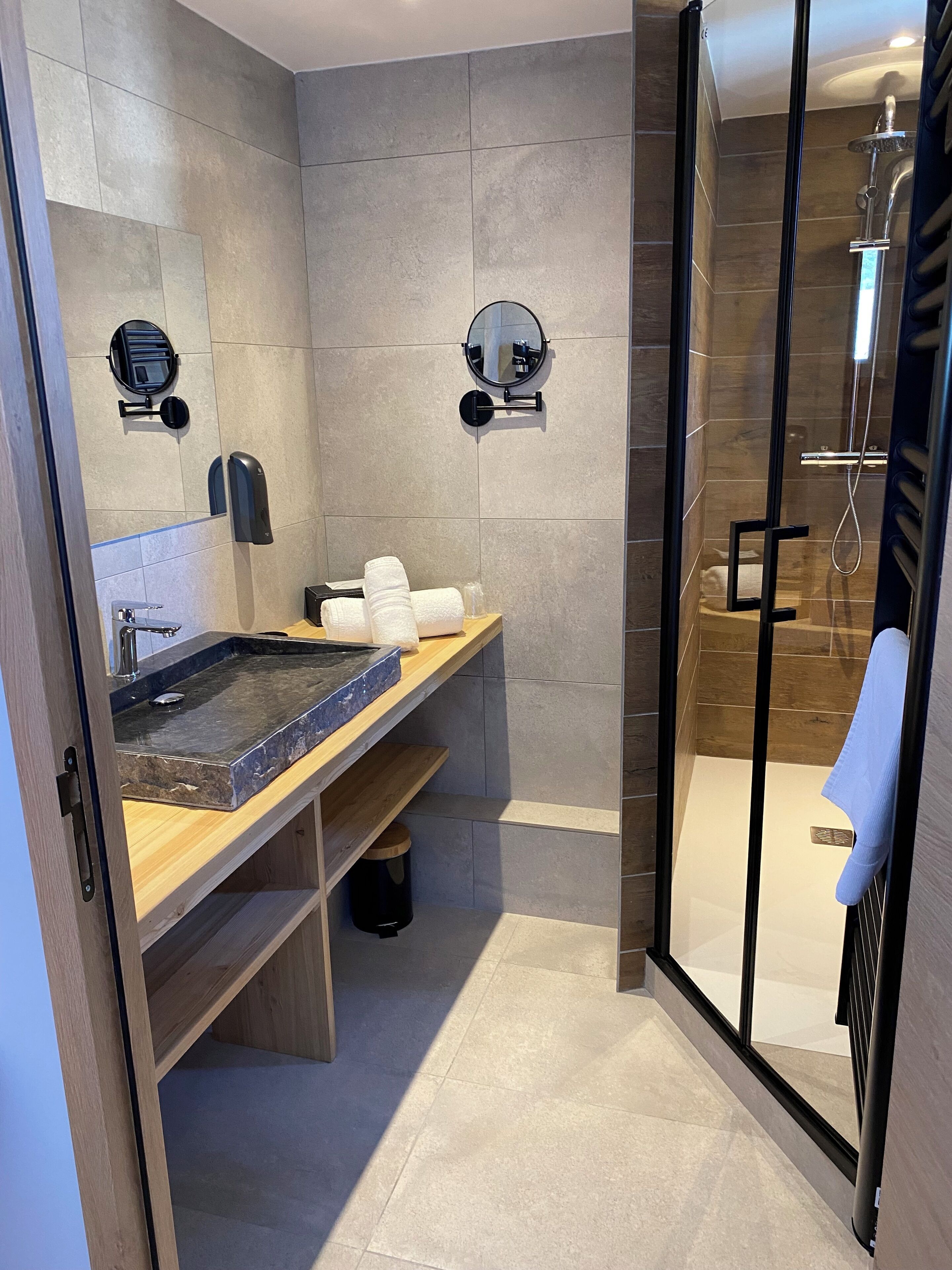 A modern bathroom with a glass-enclosed shower, a marble sink, and a wooden vanity.
