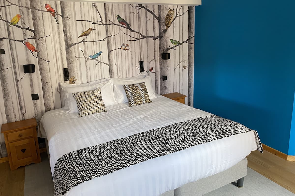 A bedroom with a bed, two nightstands, a blue accent wall, and a mural of birds on the wall.