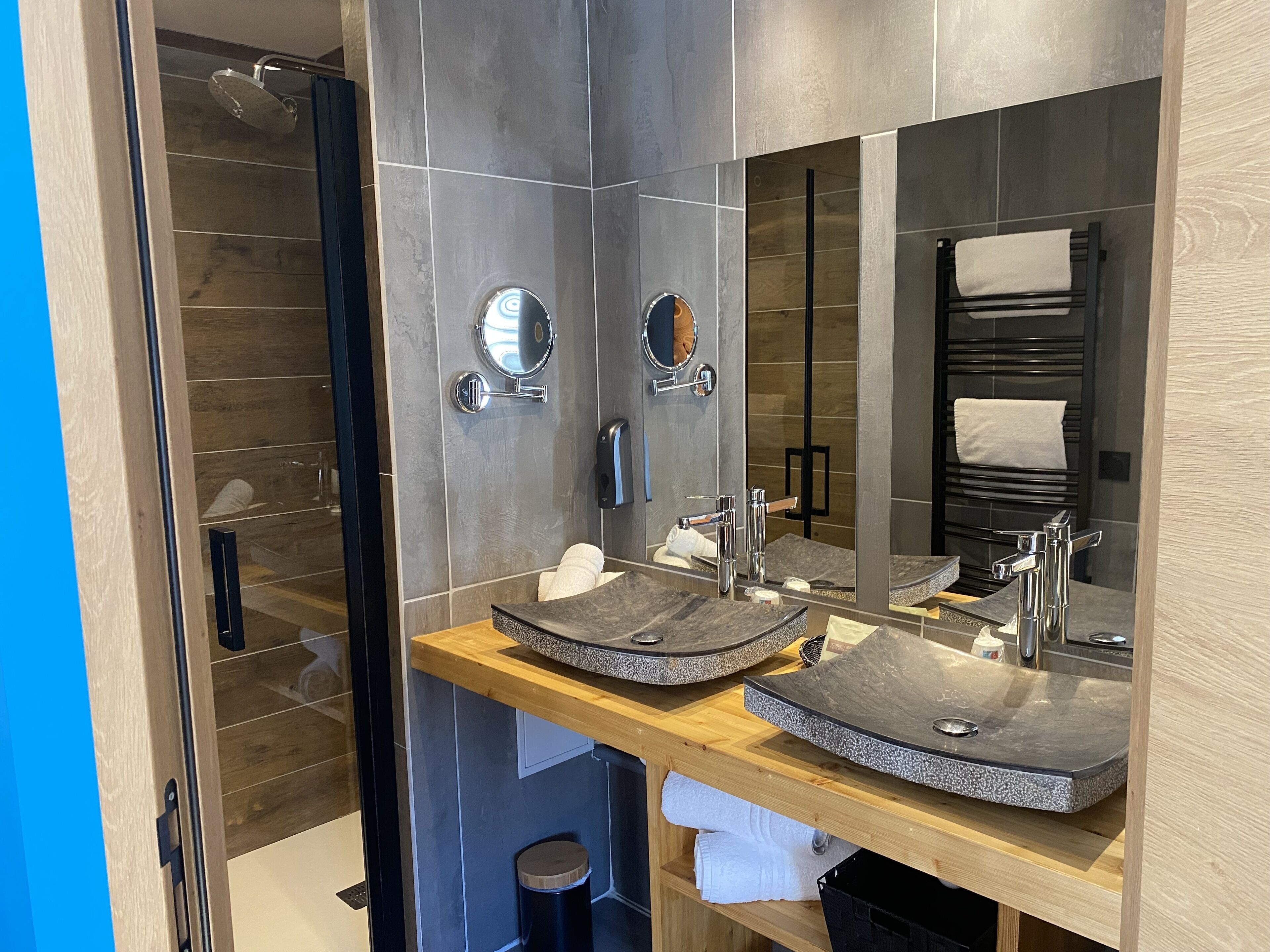 Un baño moderno con cabina de ducha de vidrio, tocador de madera con dos lavamanos y un espejo grande.