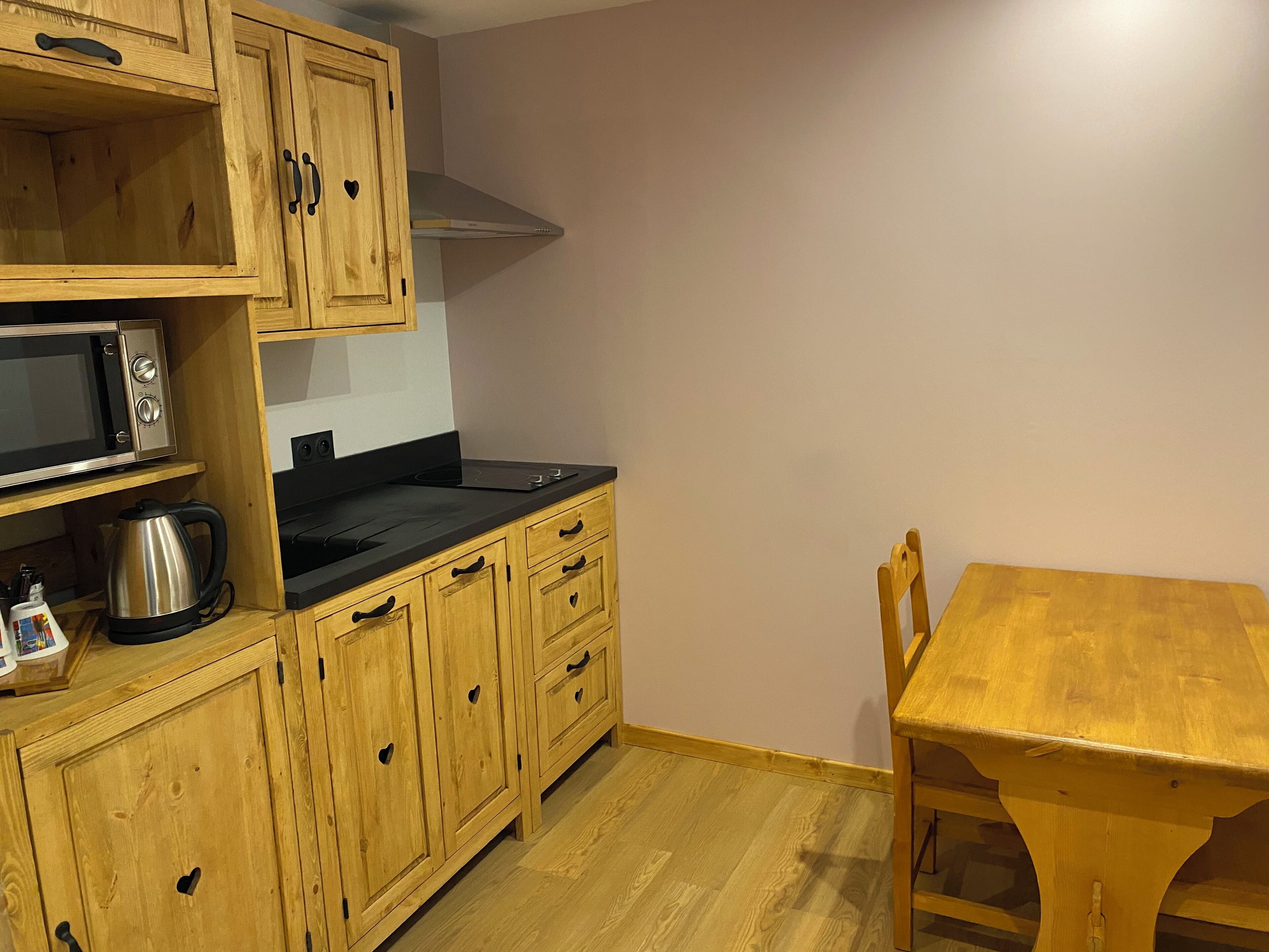A compact kitchen with wooden cabinets, a microwave, a kettle, and a wooden table.